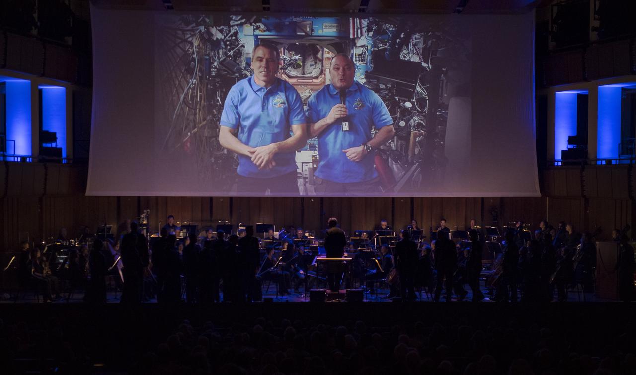 NASA astronauts Drew Feustel, left, and Scott Tingle, are seen during a video message to the audience of the "National Symphony Orchestra Pops: Space, the Next Frontier" event celebrating NASA's 60th Anniversary, Friday, June 1, 2018 at the John F. Kennedy Center for the Performing Arts in Washington. The event featured music inspired by space including artists will.i.am, Grace Potter, Coheed & Cambria, John Cho, and guest Nick Sagan, son of Carl Sagan. Photo Credit: (NASA/Aubrey Gemignani)
