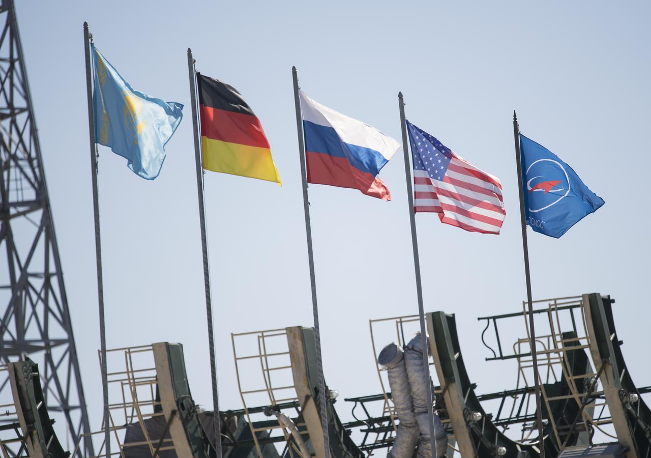 The flags of Kazakhstan, German, Russia, and the United States are seen flying after the Soyuz rocket was raised into a vertical position on the launch pad, Monday, June 4, 2018 at the Baikonur Cosmodrome in Kazakhstan. Expedition 56 Soyuz Commander Sergey Prokopyev of Roscosmos, flight engineer Serena Auñón-Chancellor of NASA, and flight engineer Alexander Gerst of ESA (European Space Agency) are scheduled to launch aboard their Soyuz MS-09 spacecraft at 7:12 a.m. Eastern time (5:12 p.m. Baikonur time), on Wednesday, June 6. Photo Credit: (NASA/Joel Kowsky)