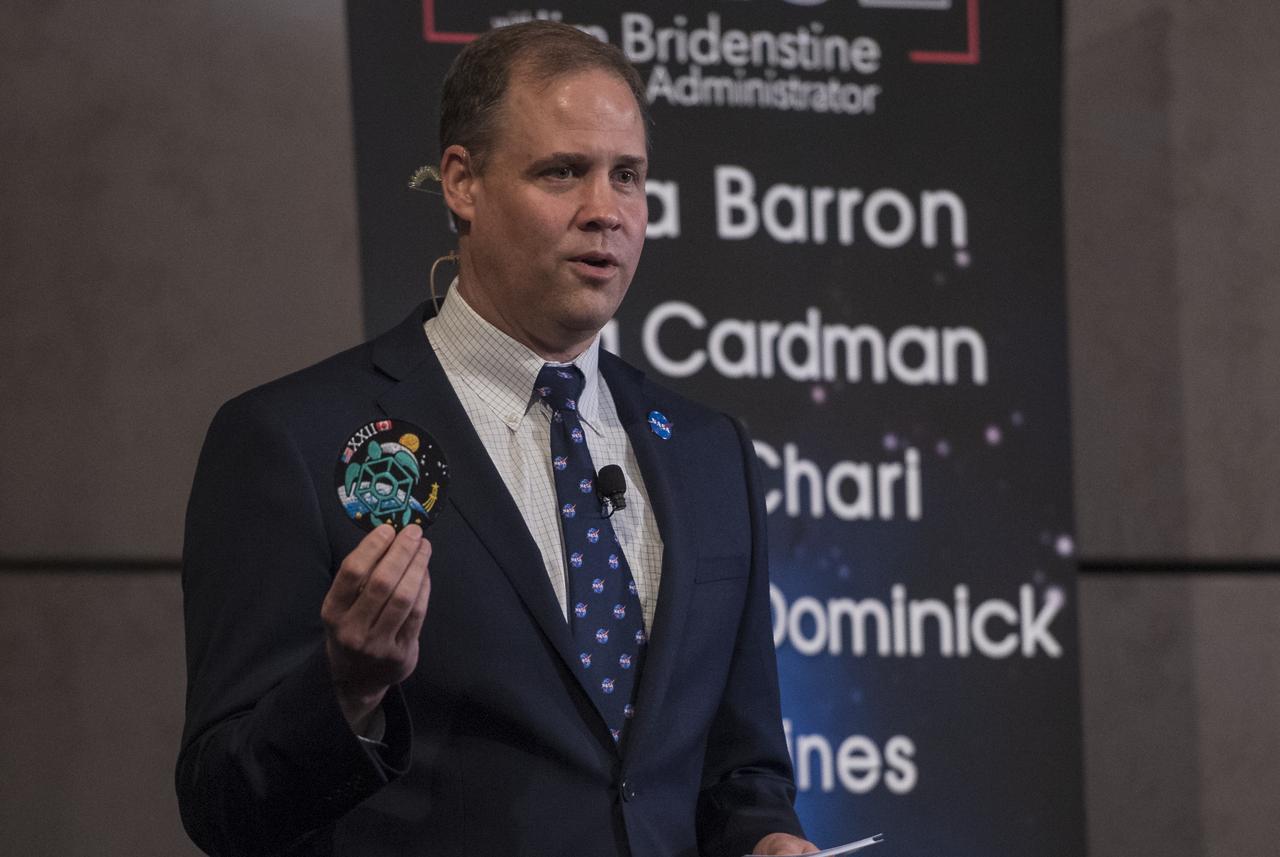 NASA Administrator Jim Bridenstine holds up the patch of the 2017 astronaut class during a live episode of the Administrator's monthly chat show, Watch This Space,  Thursday, Sept. 27, 2018 in the Webb Auditorium at NASA Headquarters in Washington. NASA's newest astronaut candidate class has started their two years of training, after which the new astronaut candidates could be assigned to missions performing research on the International Space Station, launching from American soil on spacecraft built by commercial companies, and launching on deep space missions on NASA’s new Orion spacecraft and Space Launch System rocket.  Photo Credit: (NASA/Joel Kowsky)