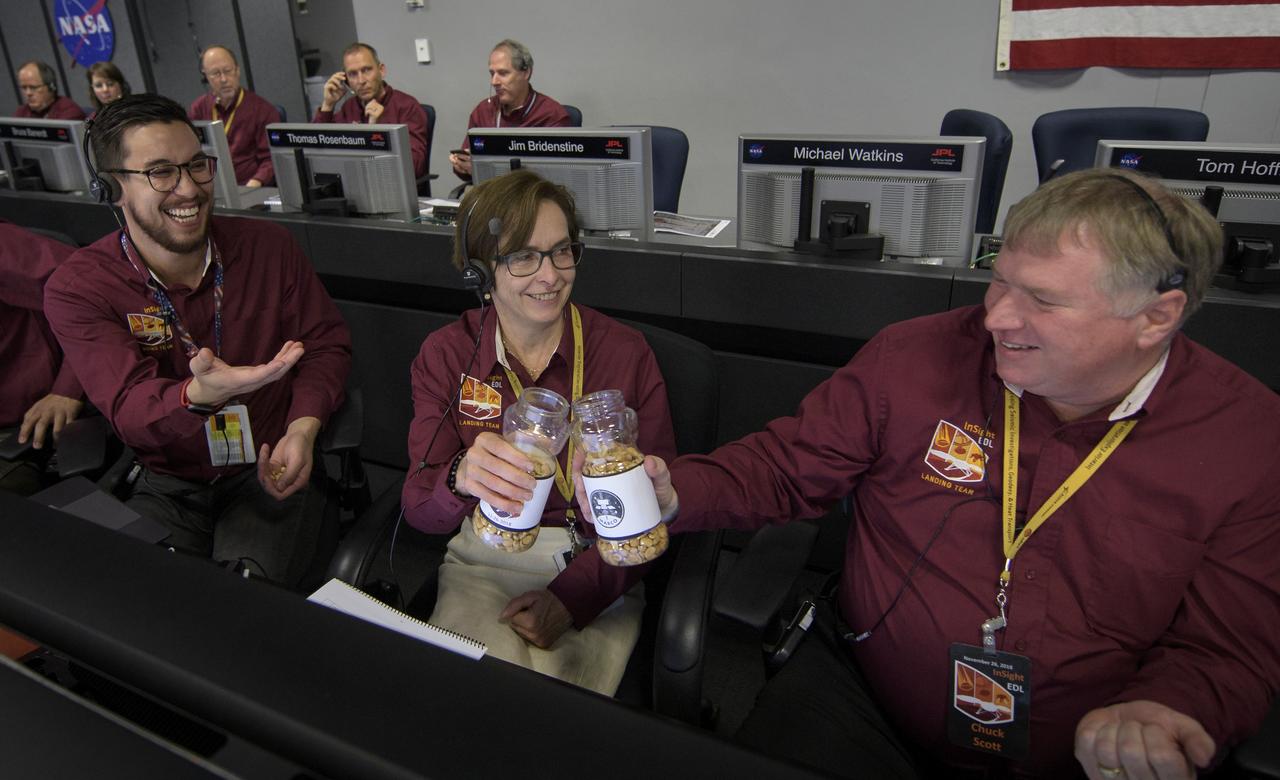 Sue Smrekar, InSight deputy principal investigator, NASA JPL, center, and Charles Scott, InSight Deputy Project Manager, NASA JPL, say cheers with two jars of good-luck peanuts as Thomas Thammasuckdi, Software Systems Engineer, NASA JPL, left, looks on, Monday, Nov. 26, 2018 inside the Mission Support Area at NASA's Jet Propulsion Laboratory in Pasadena, California. InSight, short for Interior Exploration using Seismic Investigations, Geodesy and Heat Transport, is a Mars lander designed to study the "inner space" of Mars: its crust, mantle, and core. Photo Credit: (NASA/Bill Ingalls)