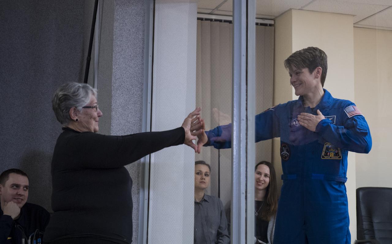 Expedition 58 Flight Engineer Anne McClain of NASA,  who is in quarantine, puts her hand up to the glass to meet her mother at the conclusion of a press conference, Sunday, Dec. 2, 2018 at the Cosmonaut Hotel in Baikonur, Kazakhstan. Launch of the Soyuz rocket is scheduled for Dec. 3 that will carry McClain, Soyuz Commander Oleg Kononenko of Roscosmos, and Flight Engineer David Saint-Jacques of the Canadian Space Agency (CSA) into orbit to begin their six and a half month mission on the International Space Station. Photo Credit: (NASA/Aubrey Gemignani).