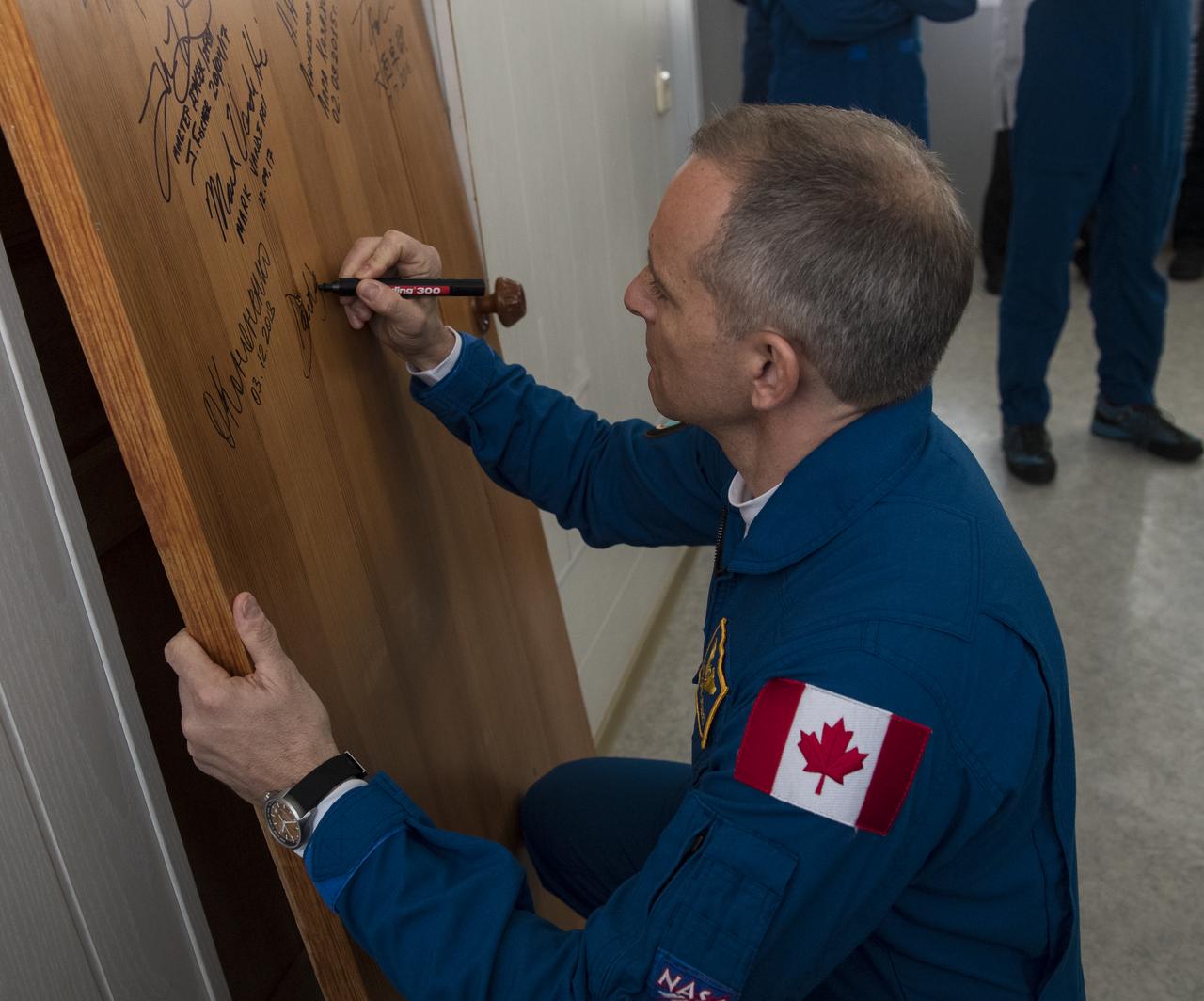 Expedition 58 Flight Engineer David Saint-Jacques of the Canadian Space Agency (CSA) performs the traditional door signing at the Cosmonaut Hotel prior to departing the hotel for launch in a Soyuz rocket with fellow crewmates, Soyuz Commander Oleg Kononenko of Roscosmos, and Flight Engineer Anne McClain of NASA, Monday, Dec. 3, 2018, in Baikonur, Kazakhstan. Launch of the Soyuz rocket is scheduled for the same day and will carry Saint-Jacques, McClain, and Kononenko into orbit to begin their six and a half month mission on the International Space Station. Photo Credit: (NASA/Aubrey Gemignani)