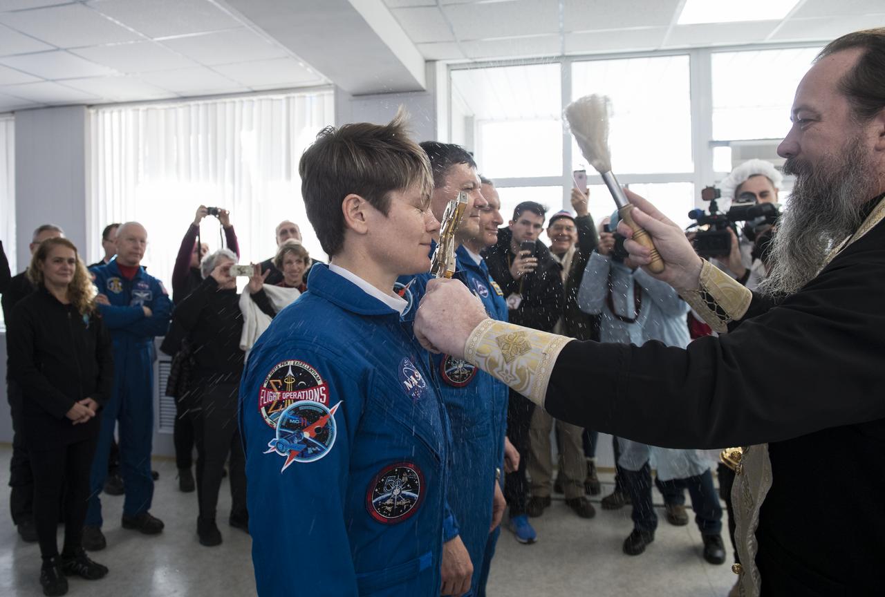 Expedition 58 Flight Engineer Anne McClain of NASA, left, receives the traditional blessing from a Russian Orthodox priest at the Cosmonaut Hotel prior to her launch on the Soyuz rocket to the International Space Station (ISS), Monday, Dec. 3, 2018, in Baikonur, Kazakhstan. She and fellow crewmates, Soyuz Commander Oleg Kononenko of Roscosmos, and Flight Engineer David Saint-Jacques of the Canadian Space Agency (CSA) will spend the next six and a half months living and working aboard the ISS. Photo Credit: (NASA/Aubrey Gemignani)