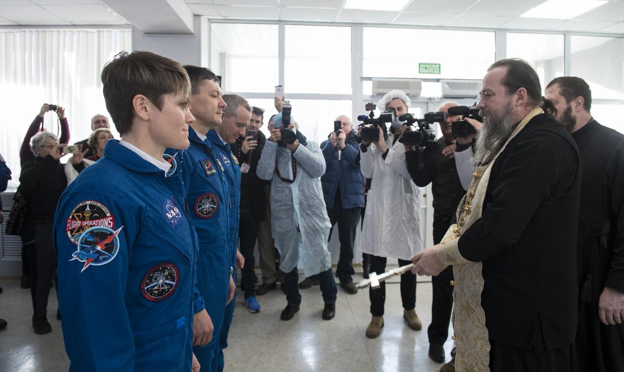 From left to right, Expedition 58 Flight Engineer Anne McClain of NASA, Soyuz Commander Oleg Kononenko of Roscosmos, and Flight Engineer David Saint-Jacques of the Canadian Space Agency (CSA), receive the traditional blessing from a Russian Orthodox priest at the Cosmonaut Hotel prior to their launch on the Soyuz rocket to the International Space Station (ISS), Monday, Dec. 3, 2018, in Baikonur, Kazakhstan. They will spend the next six and a half months living and working aboard the ISS. Photo Credit: (NASA/Aubrey Gemignani)