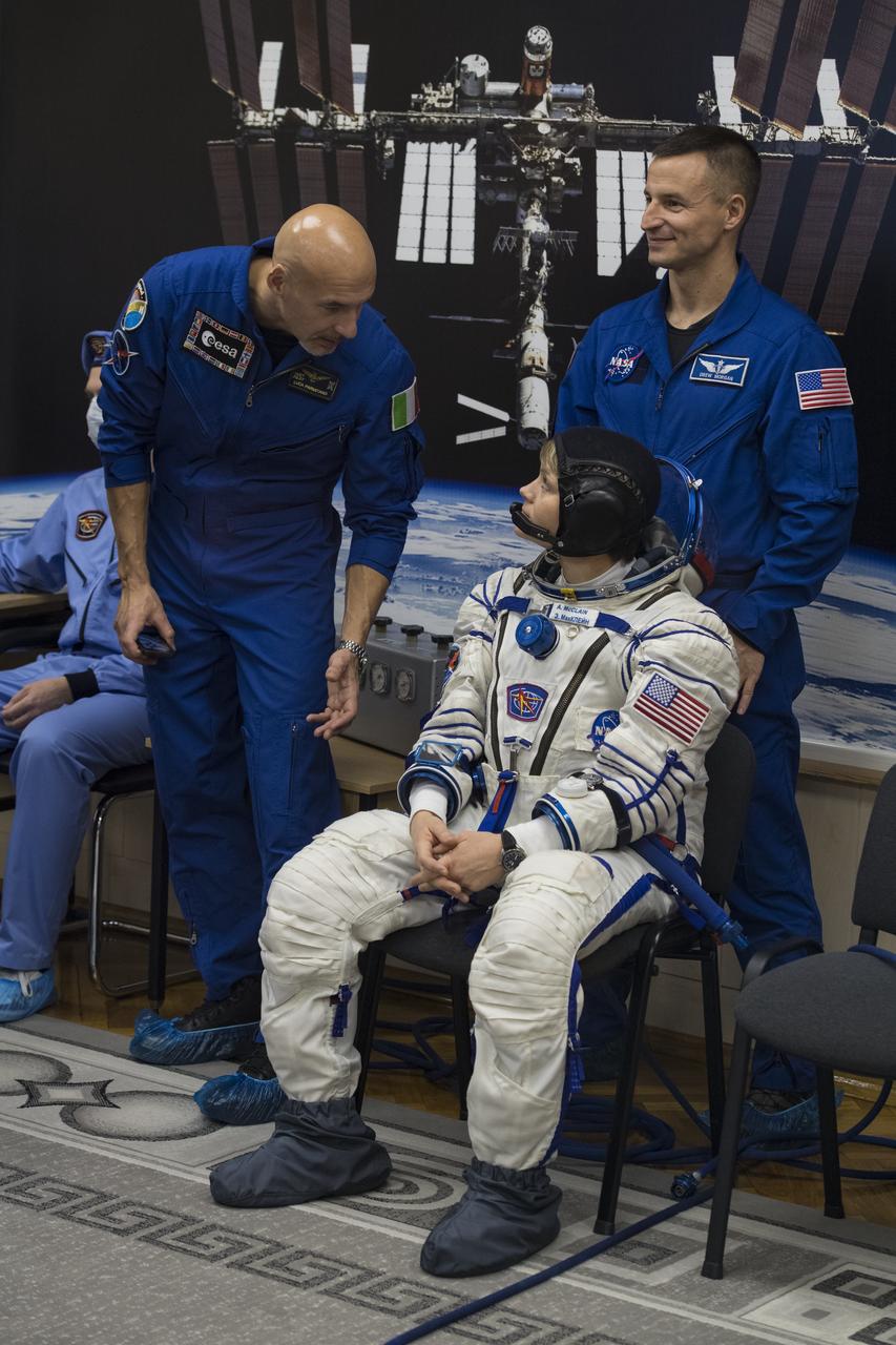 Expedition 58 Flight Engineer Anne McClain of NASA speaks with backup crew member Luca Parmitano of ESA (European Space Agency) while she waits to have her Russian Sokol suit pressure checked in preparation for her launch aboard the Soyuz MS-11 spacecraft on Monday, Dec. 3, 2018, at the Baikonur Cosmodrome in Kazakhstan. Launch of the Soyuz rocket is scheduled for the same day and will carry McClain, Soyuz Commander Oleg Kononenko of Roscosmos, and Flight Engineer David Saint-Jacques of the Canadian Space Agency (CSA) into orbit to begin their six and a half month mission on the International Space Station. Photo Credit: (NASA/Aubrey Gemignani)