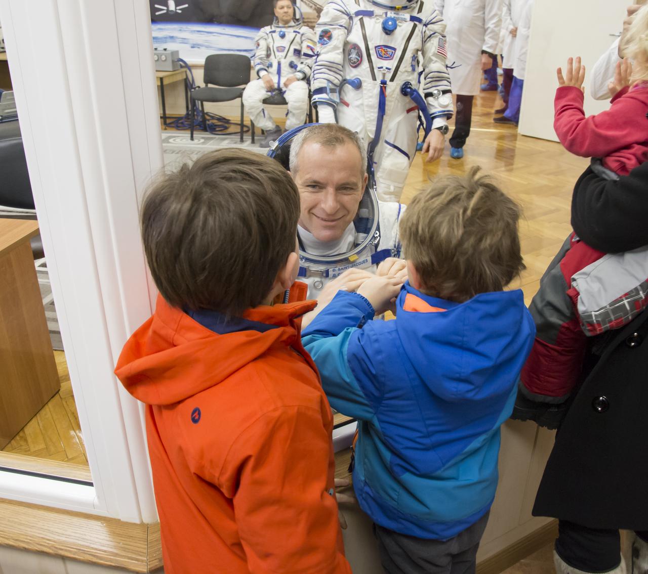 Expedition 58 Flight Engineer David Saint-Jacques of the Canadian Space Agency (CSA) puts his hands up to the glass, to meet his sons while in quarantine, after having his Russian Sokol suit pressure checked in preparation for his launch aboard the Soyuz MS-11 spacecraft on Monday, Dec. 3, 2018, at the Baikonur Cosmodrome in Kazakhstan. Launch of the Soyuz rocket is scheduled for the same day and will carry Saint-Jacques, Soyuz Commander Oleg Kononenko of Roscosmos, and Flight Engineer Anne McClain of NASA, and into orbit to begin their six and a half month mission on the International Space Station. Photo Credit: (NASA/Victor Zelentsov)