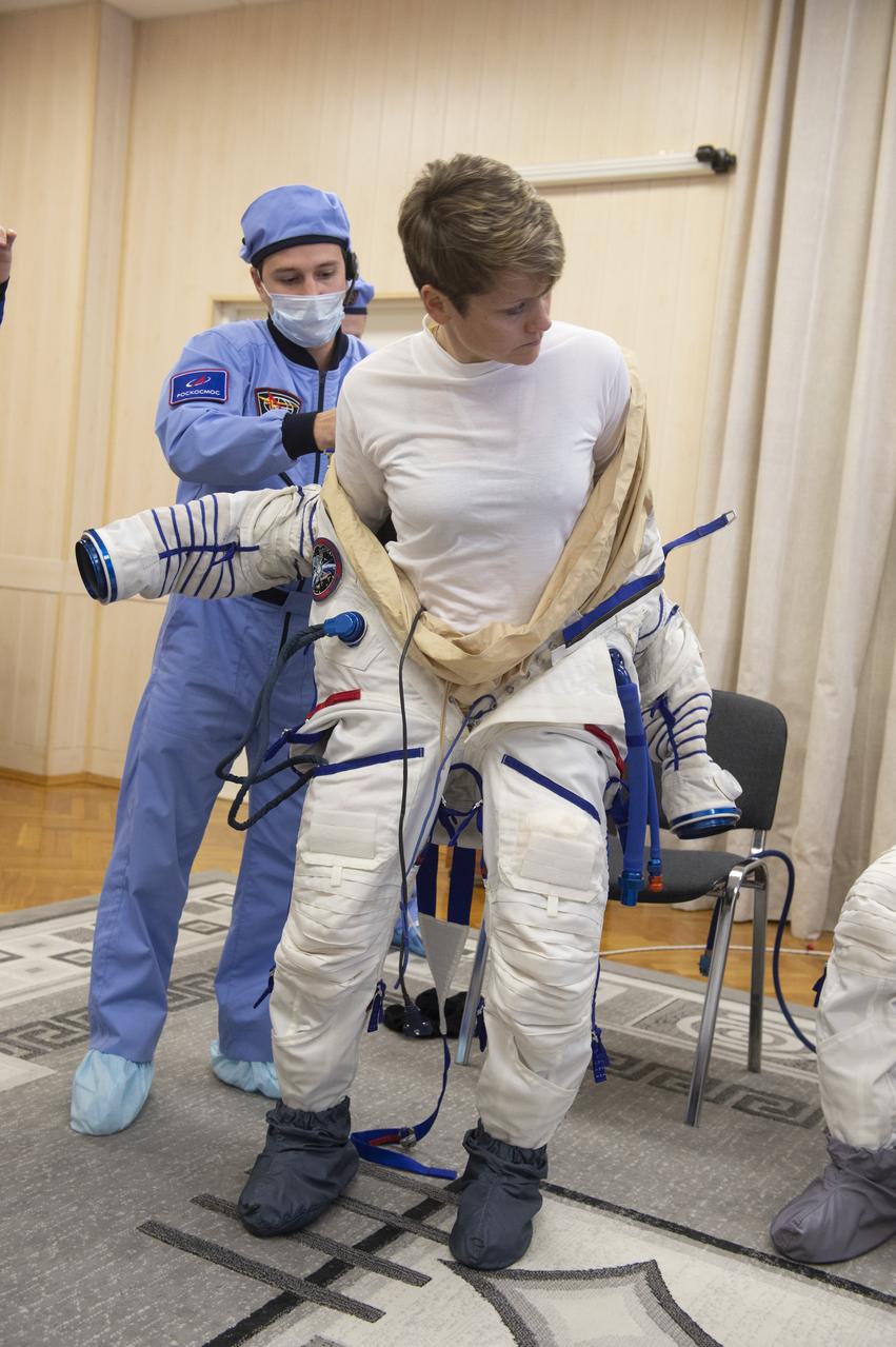 Flight Engineer Anne McClain of NASA is helped into her Russian Sokol suit as she and fellow crewmates, Expedition 58 Soyuz Commander Oleg Kononenko of Roscosmos and Flight Engineer David Saint-Jacques of the Canadian Space Agency (CSA) prepare for their Soyuz launch to the International Space Station, on Monday, Dec. 3, 2018 at the Baikonur Cosmodrome in Kazakhstan. Launch of the Soyuz rocket is scheduled for the same day and will carry McClain, Kononenko, and Saint-Jacques into orbit to begin their six and a half month mission on the International Space Station. Photo Credit: (GCTC/NASA/Andrey Shelepin)