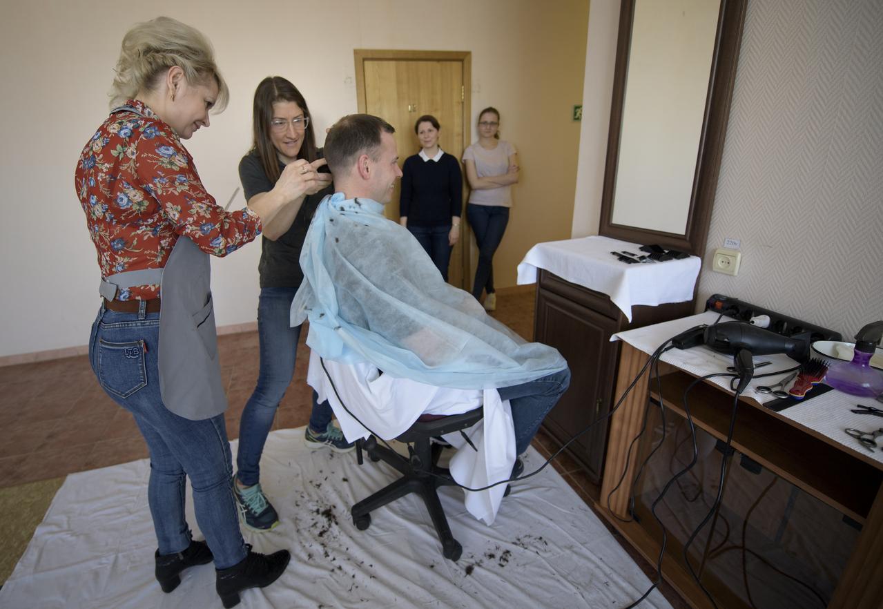 Expedition 59 astronaut Nick Hague of NASA sits as fellow crewmember, astronaut Christina Koch of NASA, is shown how to cut hair by a stylist, Tuesday, March 12, 2019 at the Cosmonaut Hotel in Baikonur, Kazakhstan. Crewmembers often give each other haircuts while onboard the International Space Station. Hague, Koch, and Alexey Ovchinin of Roscosmos, will launch March 14, U.S. time, on the Soyuz MS-12 spacecraft from the Baikonur Cosmodrome for a six-and-a-half month mission on the International Space Station. Photo Credit: (NASA/Bill Ingalls)