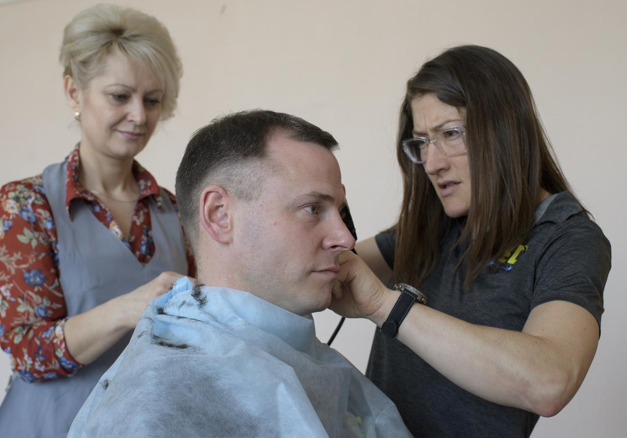 Expedition 59 astronaut Nick Hague of NASA sits as fellow crewmember, astronaut Christina Koch of NASA, right, is shown how to cut hair by a stylist, Tuesday, March 12, 2019 at the Cosmonaut Hotel in Baikonur, Kazakhstan. Crewmembers often give each other haircuts while onboard the International Space Station. Hague, Koch, and Alexey Ovchinin of Roscosmos, will launch March 14, U.S. time, on the Soyuz MS-12 spacecraft from the Baikonur Cosmodrome for a six-and-a-half month mission on the International Space Station. Photo Credit: (NASA/Bill Ingalls)
