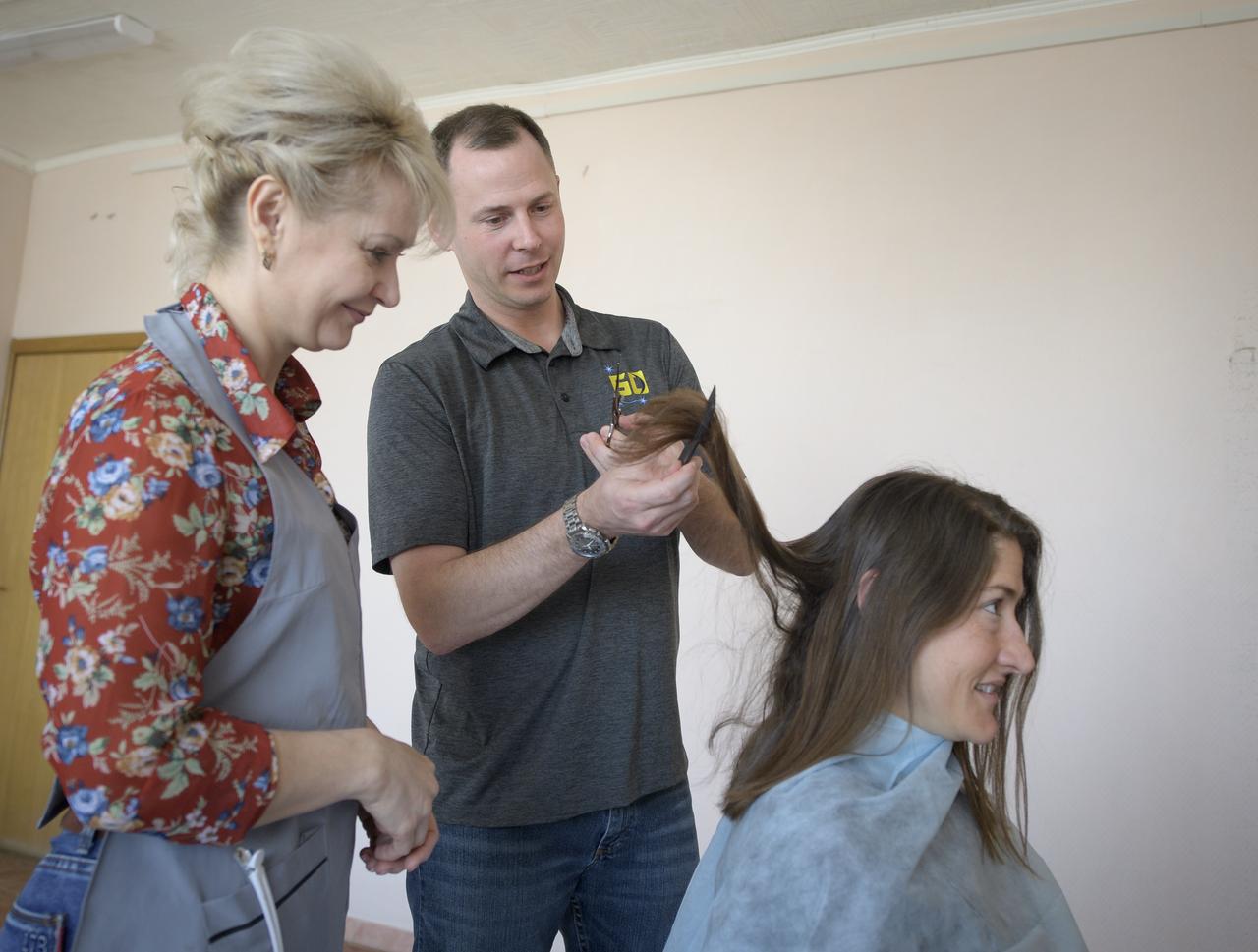Expedition 59 astronaut Christina Koch of NASA sits as fellow crewmember, astronaut Nick Hague of NASA, is shown how to cut hair by a stylist, Tuesday, March 12, 2019 at the Cosmonaut Hotel in Baikonur, Kazakhstan. Crewmembers often give each other haircuts while onboard the International Space Station. Hague, Koch, and Alexey Ovchinin of Roscosmos, will launch March 14, U.S. time, on the Soyuz MS-12 spacecraft from the Baikonur Cosmodrome for a six-and-a-half month mission on the International Space Station. Photo Credit: (NASA/Bill Ingalls)