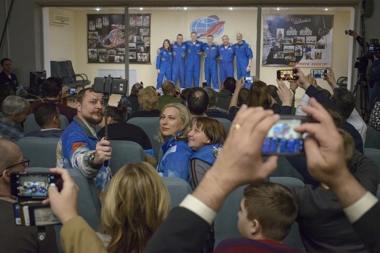 Press, family, and friends take photos as the Expedition 59 prime and backup crews pose at the conclusion of a press conference, Wednesday, March 13, 2019 at the Cosmonaut Hotel in Baikonur, Kazakhstan. Expedition 59 crewmembers Nick Hague and Christina Koch of NASA, along with Alexey Ovchinin of Roscosmos will launch March 14, U.S. time, on the Soyuz MS-12 spacecraft from the Baikonur Cosmodrome for a six-and-a-half month mission on the International Space Station. Photo Credit: (NASA/Bill Ingalls)