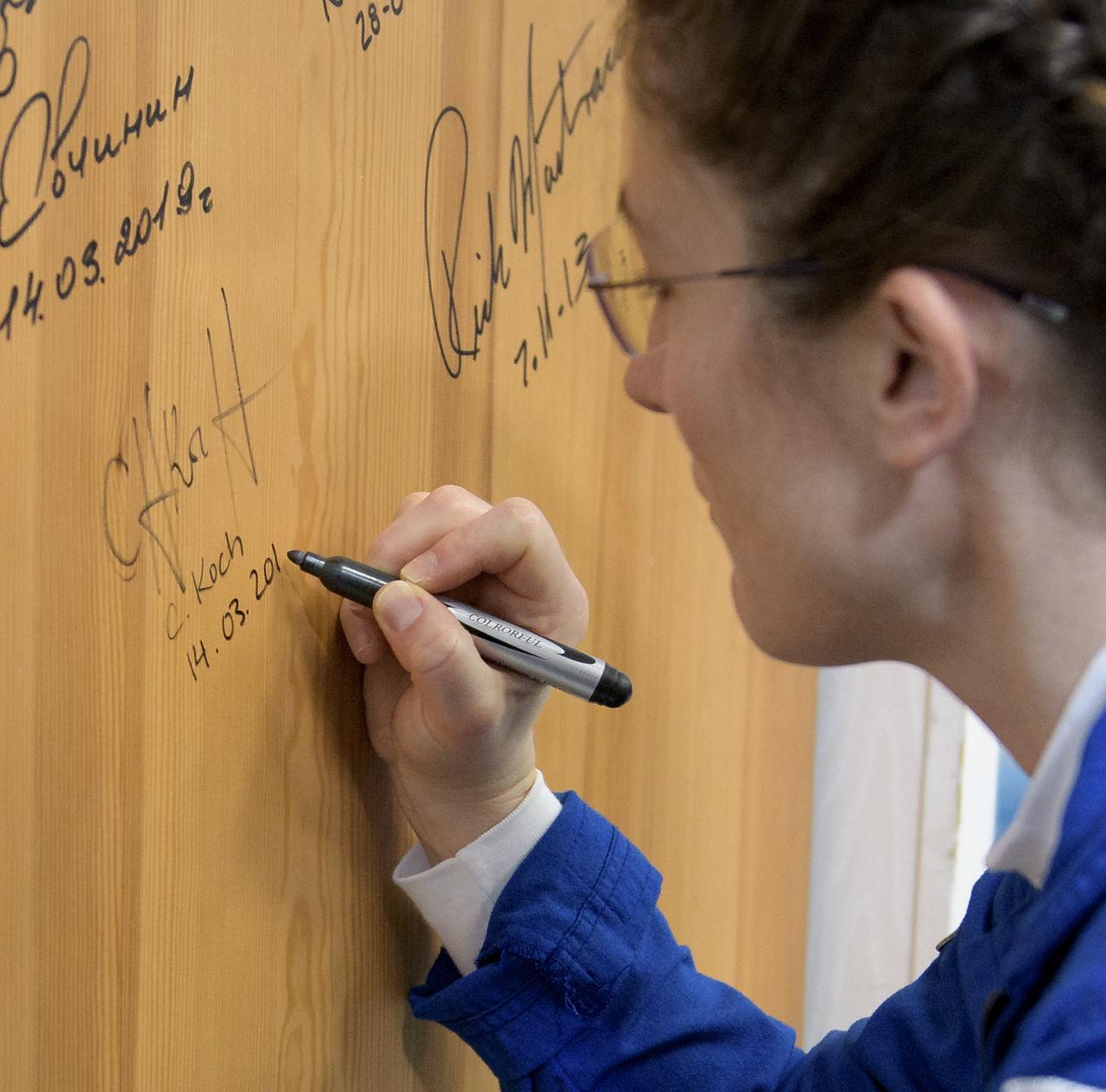 Expedition 59 astronaut Christina Koch of NASA signs a door in the Cosmonaut Hotel prior to departing for launch on a Soyuz rocket with Nick Hague of NASA, and Alexey Ovchinin of Roscosmos, Thursday, March 14, 2019 in Baikonur, Kazakhstan. Hague, Koch, and Ovchinin will launch March 14, U.S. time, on the Soyuz MS-12 spacecraft from the Baikonur Cosmodrome for a six-and-a-half month mission on the International Space Station. Photo Credit: (NASA/Bill Ingalls)