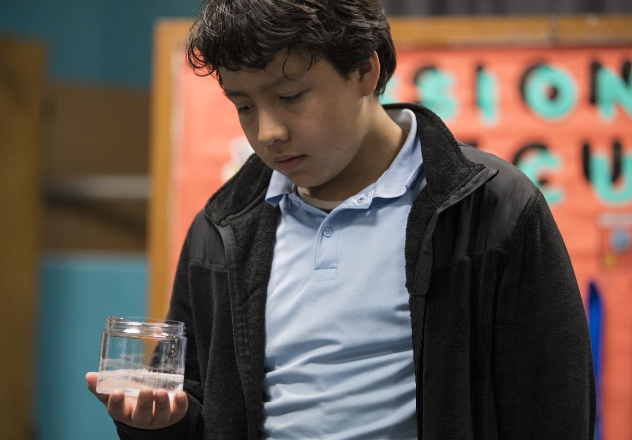 A student observes a glass of water with an Alka-Seltzer tab in it while conducting an experiment on effervescence, Friday, May 3, 2019 at the Challenger Center in Lanham, MD. NASA astronaut Ricky Arnold helped them carry out the experiment which he also conducted during his 197 day mission onboard the International Space Station (ISS) during Expeditions 55/56. Photo Credit: (NASA/Aubrey Gemignani)