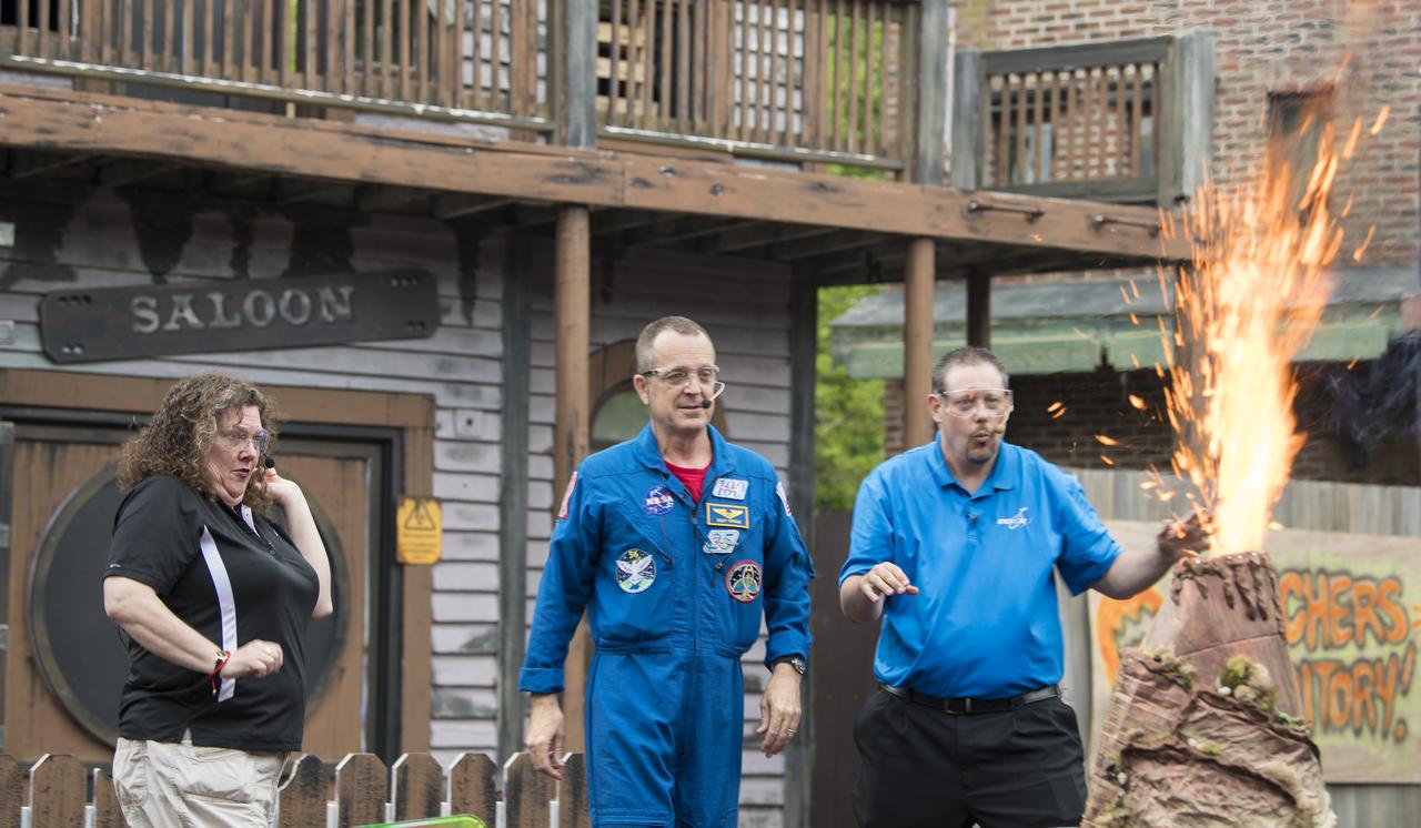 NASA astronaut Ricky Arnold, center, and Smithsonian National Air and Space Museum's Beth Wilson, left, and Marty Kelsey, right, jump backwards as a model volcano erupts with fire during a Stem in 30 segment, Friday, May 3, 2019 at Six Flags America theme park in Upper Marlboro, MD. During Expedition 55/56, Arnold completed three spacewalks for a total of 19.5 hours outside the space station, and concluded his 197 day mission when he landed in a remote area near the town of Zhezkazgan, Kazakhstan in Oct. 2018. He also flew to the space station on shuttle mission STS-119 to deliver the final pair of power-generating solar array wings. Photo Credit: (NASA/Aubrey Gemignani)