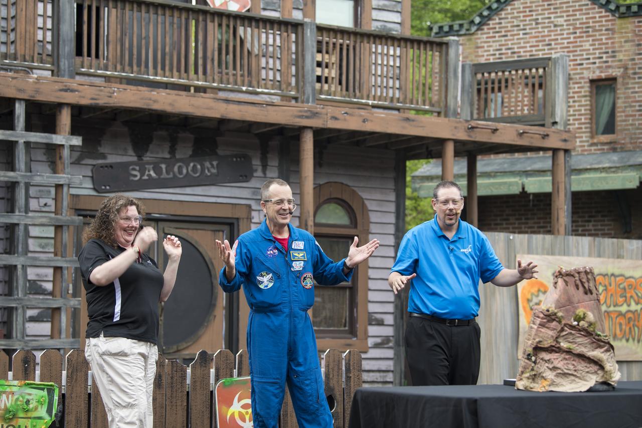 NASA astronaut Ricky Arnold, center, and Smithsonian National Air and Space Museum's Beth Wilson, left, and Marty Kelsey, right, react after a model volcano erupted with fire during a Stem in 30 segment, Friday, May 3, 2019 at Six Flags America theme park in Upper Marlboro, MD. During Expedition 55/56, Arnold completed three spacewalks for a total of 19.5 hours outside the space station, and concluded his 197 day mission when he landed in a remote area near the town of Zhezkazgan, Kazakhstan in Oct. 2018. He also flew to the space station on shuttle mission STS-119 to deliver the final pair of power-generating solar array wings. Photo Credit: (NASA/Aubrey Gemignani)