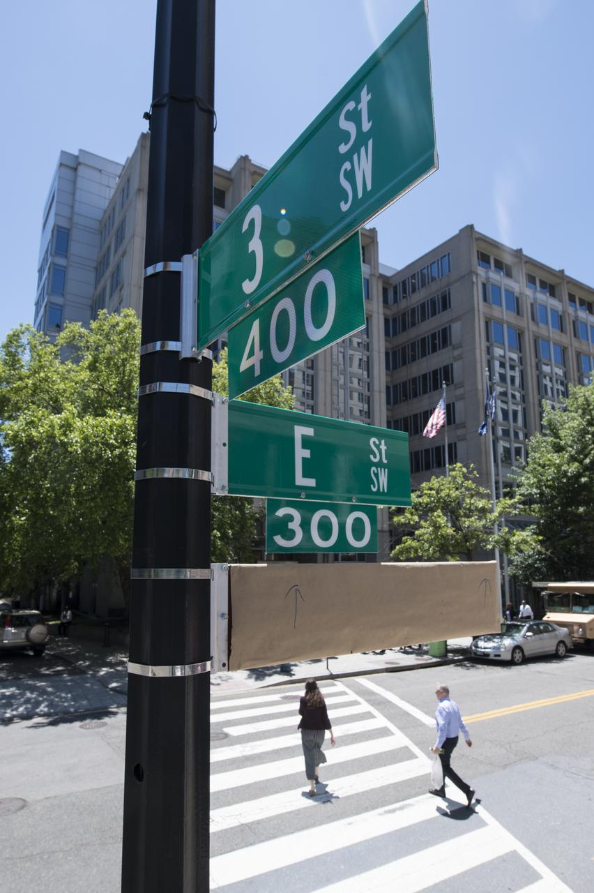 A covered street sign is seen outside of the NASA Headquarters building the day before a street renaming ceremony, Tuesday, June 11, 2019 in Washington, DC. On Wednesday, June 12, a ceremony was held to dedicate the 300 block of E Street SW in front of the NASA Headquarters building as "Hidden Figures Way" to honor Katherine Johnson, Dorothy Vaughan, Mary Jackson and all women who have dedicated their lives to honorably serving their country, advancing equality, and contributing to the space program of the United States. Photo Credit: (NASA/Joel Kowsky)