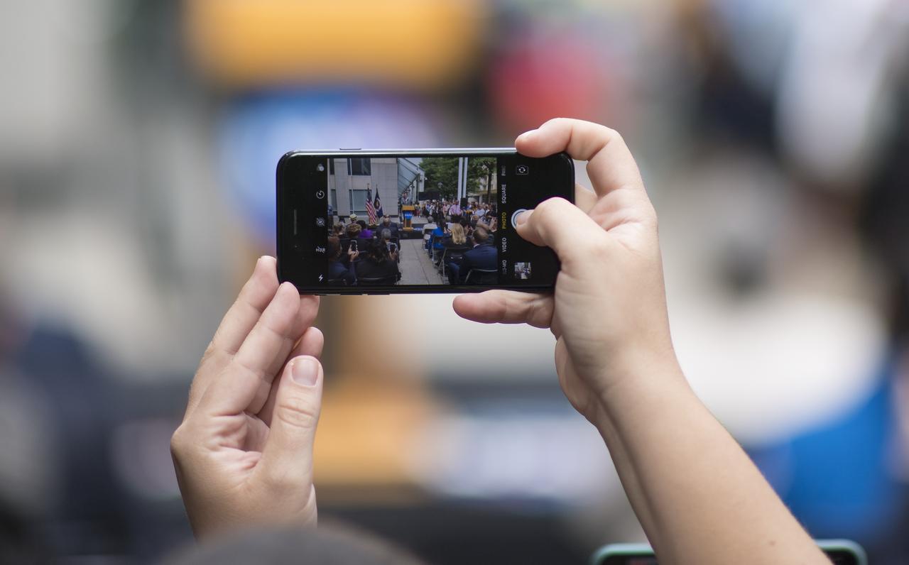 A member of the audience takes a picture with their cell phone as U.S. Senator Ted Cruz, R-Texas, delivers remarks during the dedication ceremony for "Hidden Figures Way," Wednesday, June 12, 2019 at NASA Headquarters in Washington, DC. The 300 block of E Street SW in front of the NASA Headquarters building was designated as "Hidden Figures Way" to honor Katherine Johnson, Dorothy Vaughan, Mary Jackson and all women who have dedicated their lives to honorably serving their country, advancing equality, and contributing to the space program of the United States. Photo Credit: (NASA/Joel Kowsky)