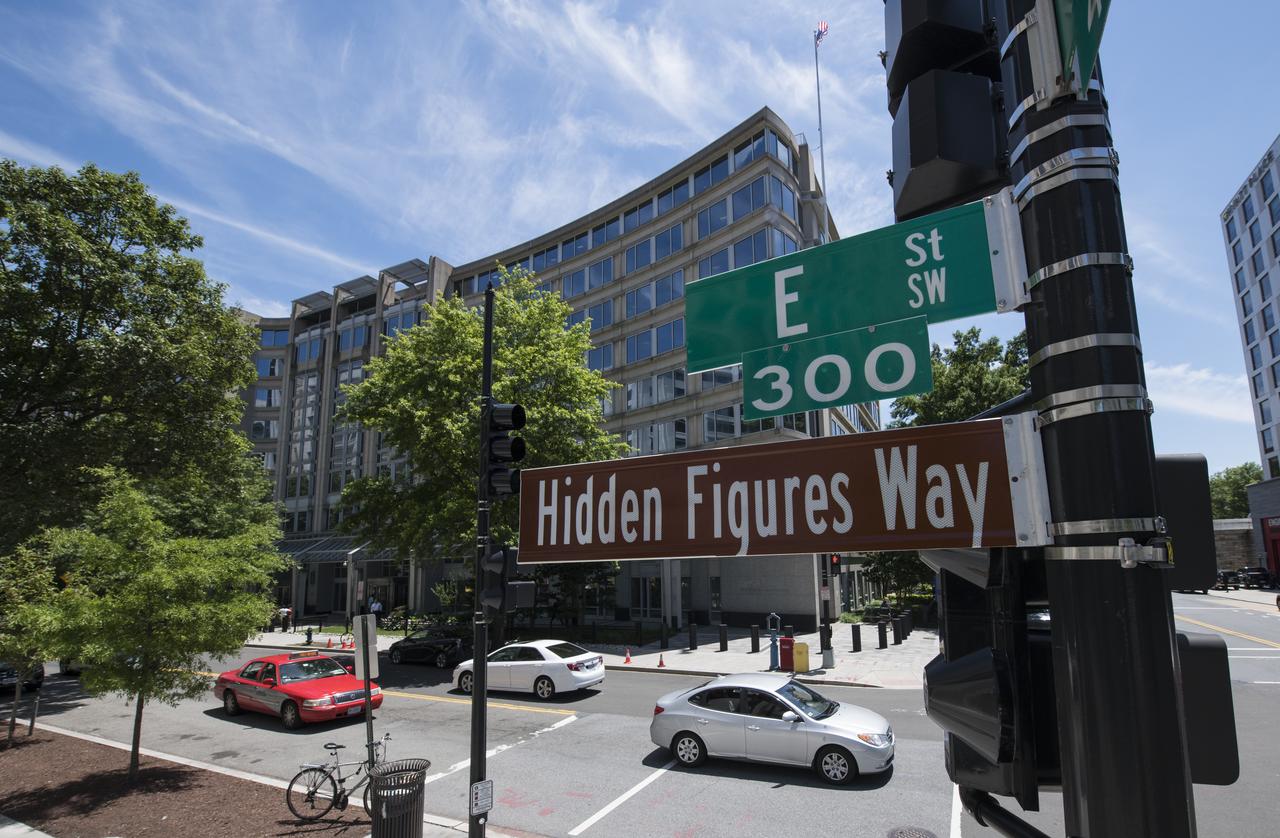 A "Hidden Figures Way" street sign is seen at the corner of 4th and E Street SW across from the NASA Headquarters building following a dedication ceremony, Wednesday, June 12, 2019 in Washington, DC. The 300 block of E Street SW in front of the NASA Headquarters building was designated as "Hidden Figures Way" to honor Katherine Johnson, Dorothy Vaughan, Mary Jackson and all women who have dedicated their lives to honorably serving their country, advancing equality, and contributing to the space program of the United States. Photo Credit: (NASA/Joel Kowsky)