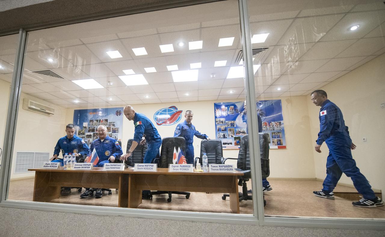 Expedition 60 prime crew members flight engineer Andrew Morgan of NASA, left, Soyuz Commander Alexander Skvortsov of Roscosmos, second from left, and flight engineer Luca Parmitano of ESA (European Space Agency), third from left, are seen with backup crew members Sergey Ryzhikov of Roscosmos, third from right, Thomas Marshburn of NASA, second from right, and Soichi Noguchi of the Japan Aerospace Exploration Agency (JAXA), right are seen in quarantine, behind glass, as they arrive for a press conference, Friday, July 19, 2019 at the Cosmonaut Hotel in Baikonur, Kazakhstan. Expedition 60 Soyuz Commander Alexander Skvortsov of Roscosmos, flight engineer Andrew Morgan of NASA, and flight engineer Luca Parmitano of ESA (European Space Agency) are scheduled to launch to the International Space Station aboard the Soyuz MS-13 spacecraft at 12:28 p.m. Eastern time (9:28 p.m. Baikonur time) on Saturday, July 20.  Photo Credit: (NASA/Joel Kowsky)