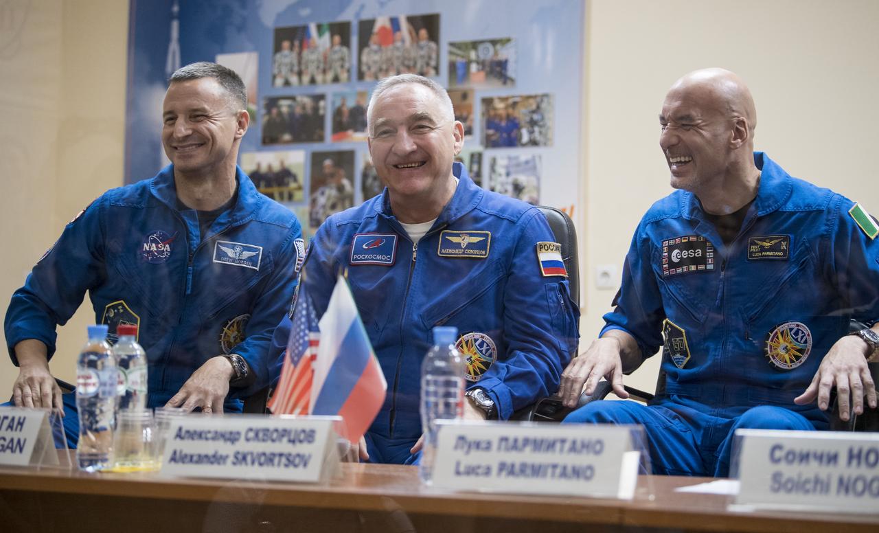 Expedition 60 flight engineer Andrew Morgan of NASA, left, Soyuz Commander Alexander Skvortsov of Roscosmos, center, and flight engineer Luca Parmitano of ESA (European Space Agency), right, are seen in quarantine, behind glass, during a press conference, Friday, July 19, 2019 at the Cosmonaut Hotel in Baikonur, Kazakhstan. Morgan, Skvortsov, and Parmitano are scheduled to launch to the International Space Station aboard the Soyuz MS-13 spacecraft at 12:28 p.m. Eastern time (9:28 p.m. Baikonur time) on Saturday, July 20. Photo Credit: (NASA/Joel Kowsky)