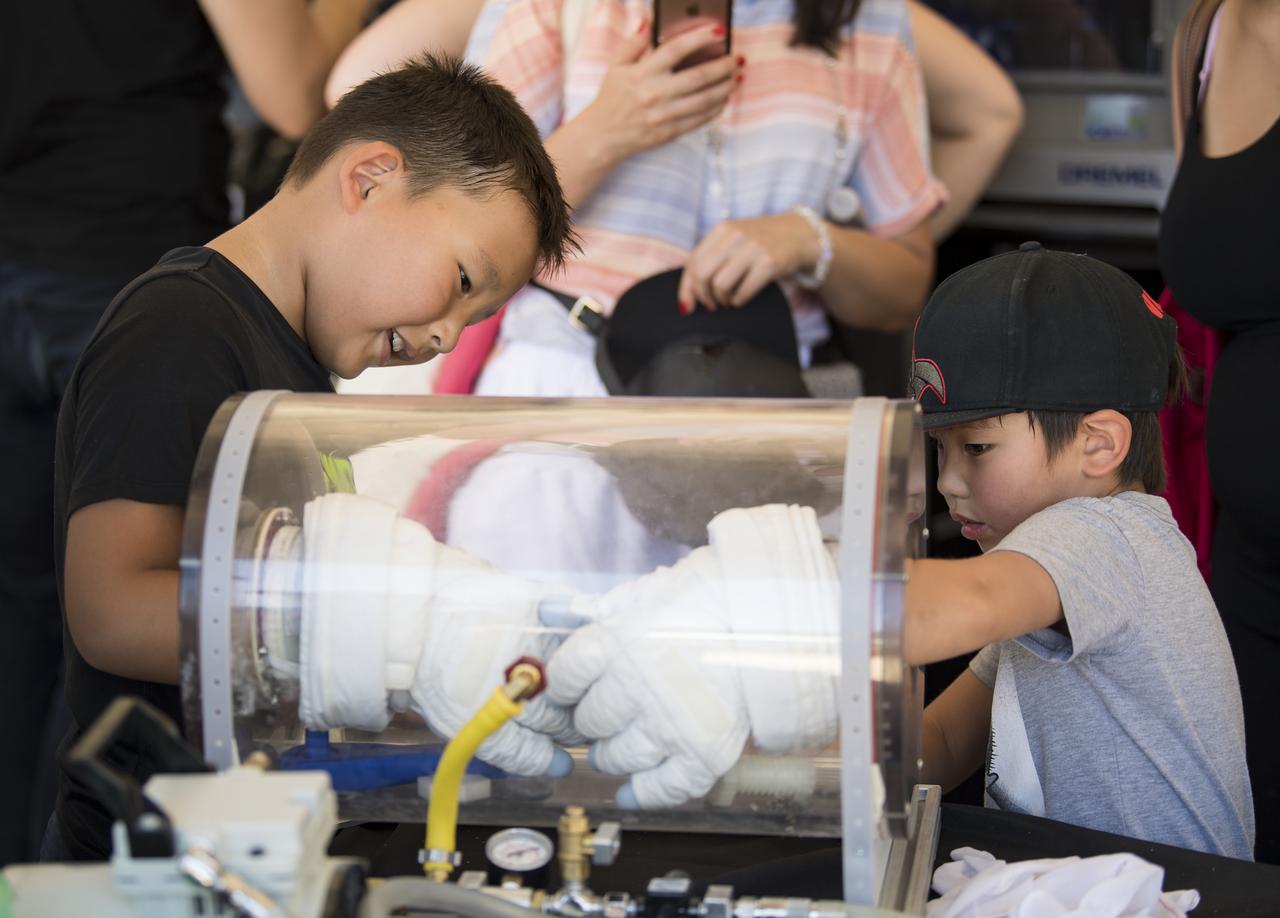 Visitors test out some space gloves at the Apollo 11 50th Anniversary celebration on the National Mall, Friday, July 19, 2019 in Washington. Apollo 11 was the first mission to land astronauts on the Moon and launched on July 16, 1969 with astronauts Neil Armstrong, Michael Collins, and Buzz Aldrin. Photo Credit: (NASA/Aubrey Gemignani)
