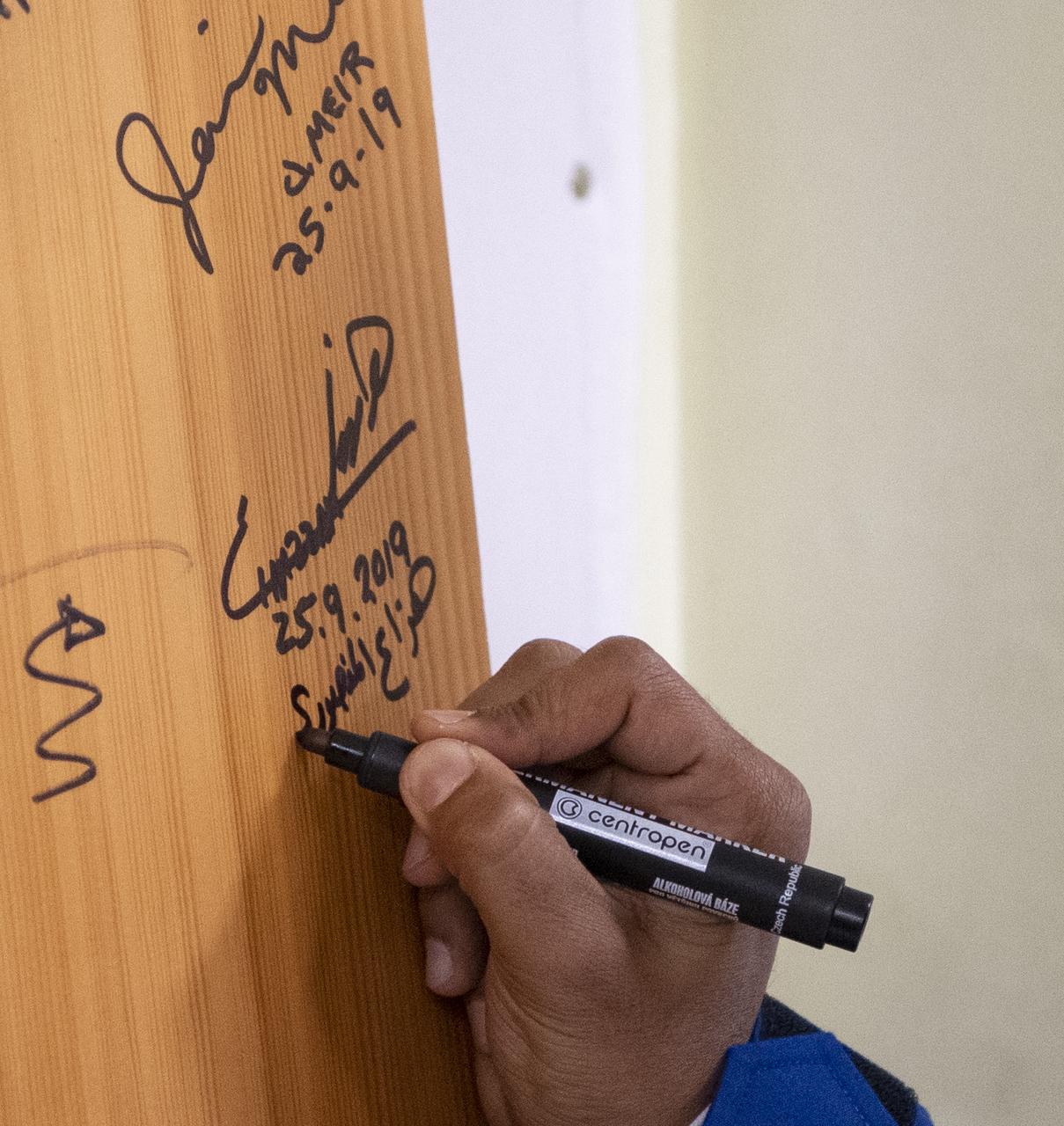 Spaceflight participant Hazzaa Ali Almansoori of the United Arab Emirates signs a door in the Cosmonaut Hotel prior to departing for launch on a Soyuz rocket with Expedition 61 crewmembers Oleg Skripochka of Roscosmos, and Jessica Meir of NASA Wednesday, Sept. 25, 2019 in Baikonur, Kazakhstan. Meir, Skripochka, and Almansoori will launch later in the day on the Soyuz MS-15 spacecraft from the Baikonur Cosmodrome to the International Space Station. Photo Credit: (NASA/Bill Ingalls)