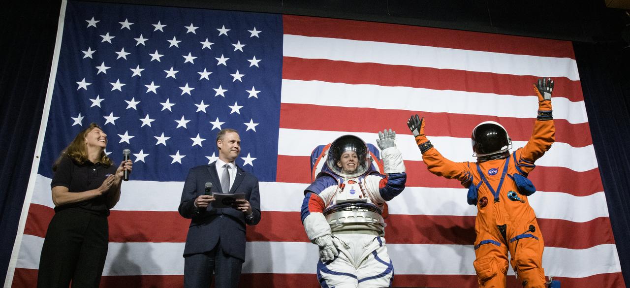 Amy Ross, a spacesuit engineer at NASA’s Johnson Space Center, left, and NASA Administrator Jim Bridenstine, second from left, watch as Kristine Davis, a spacesuit engineer at NASA’s Johnson Space Center, wearing a ground prototype of NASA’s new Exploration Extravehicular Mobility Unit (xEMU), and Dustin Gohmert, Orion Crew Survival Systems Project Manager at NASA’s Johnson Space Center, wearing the Orion Crew Survival System suit, right, wave after being introduced by the administrator, Tuesday, Oct. 15, 2019 at NASA Headquarters in Washington. The xEMU suit improves on the suits previous worn on the Moon during the Apollo era and those currently in use for spacewalks outside the International Space Station and will be worn by first woman and next man as they explore the Moon as part of the agency’s Artemis program. The Orion suit is designed for a custom fit and incorporates safety technology and mobility features that will help protect astronauts on launch day, in emergency situations, high-risk parts of missions near the Moon, and during the high-speed return to Earth.  Photo Credit: (NASA/Joel Kowsky)