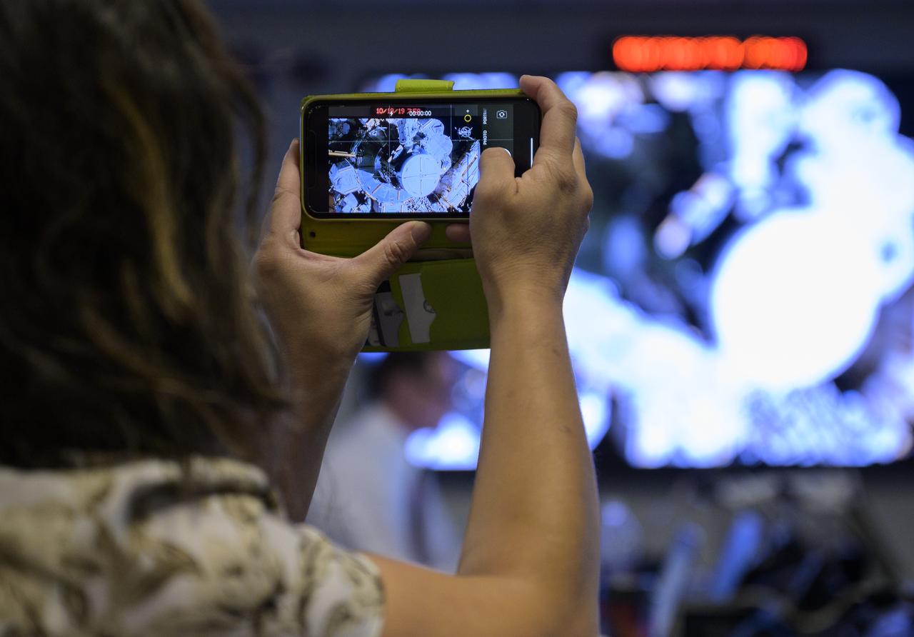 Rep. Grace Meng, D-N.Y., takes a video of a screen showing NASA astronauts Christina Koch and Jessica Meir as they venture outside the International Space Station beginning the first all-woman spacewalk on Friday, Oct. 18, 2019, in the Space Operations Center at NASA Headquarters in Washington. The first all-woman spacewalk in history began at 7:38am EDT with NASA astronauts Christina Koch and Jessica Meir venturing outside the International Space Station to replace a failed battery charge-discharge unit. This is the fourth spacewalk for Koch and Meir’s first. Photo Credit: (NASA/Joel Kowsky)