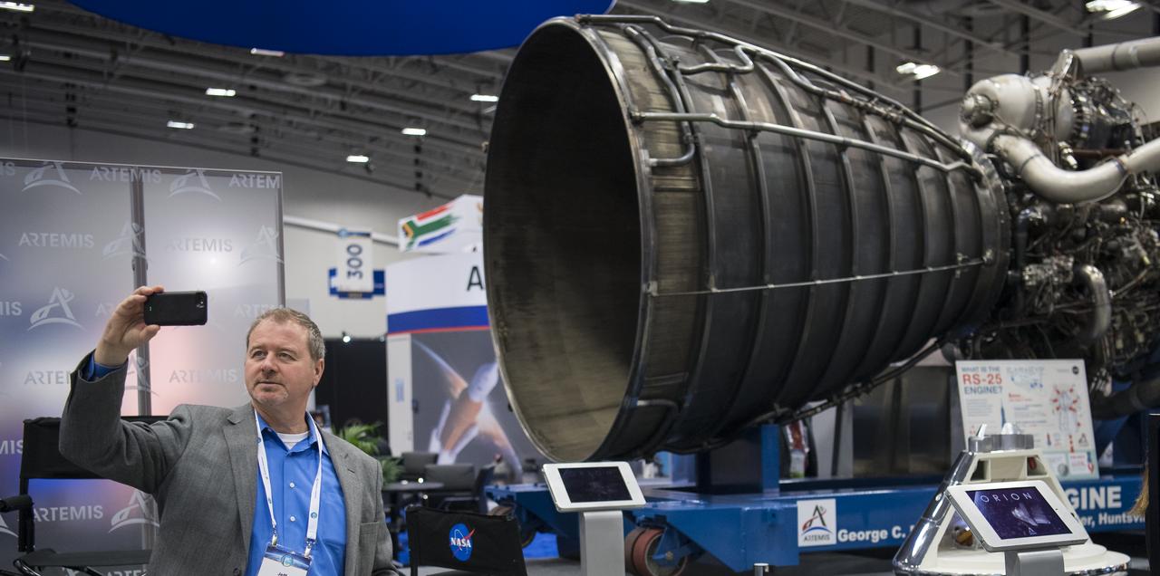 An attendee takes a selfie with an RS-25 engine, the same type that will power NASA's Space Launch System, while visiting the NASA exhibit space at the 70th International Astronautical Congress, Tuesday, Oct. 22, 2019 at the Walter E. Washington Convention Center in Washington. Photo Credit: (NASA/Joel Kowsky)