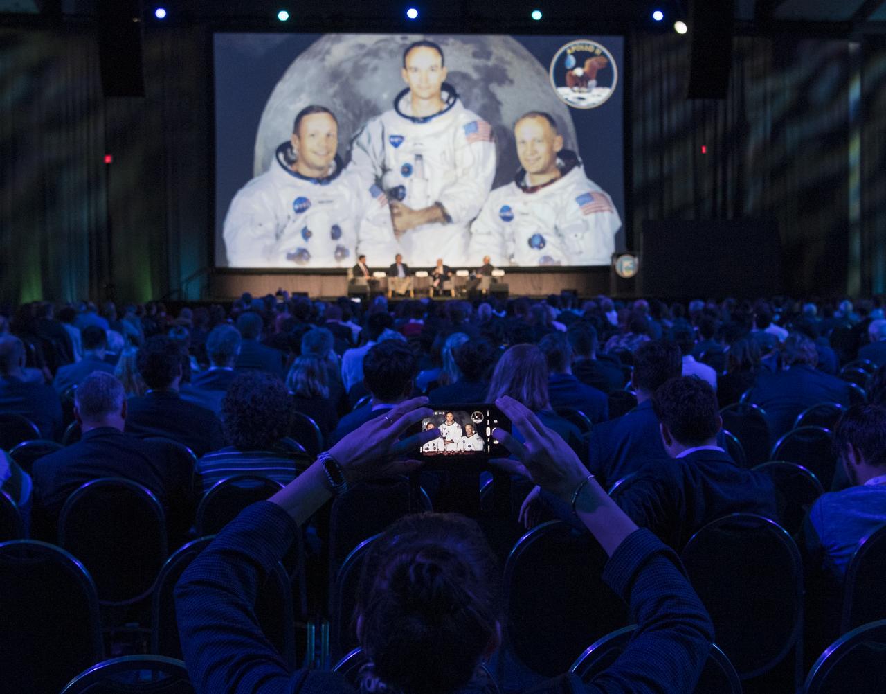 A member of the audience takes a picture of NASA astronaut Doug Wheelock, Rick Armstrong, son of Apollo 11 astronaut Neil Armstrong, Apollo 11 astronaut Buzz Aldrin, and John Logsdon, Apollo historian and Professor Emeritus at George Washington University, on stage during the International Astronautical Federation World Space Award highlight lecture at the 70th International Astronautical Congress, Thursday, Oct. 24, 2019, at the Walter E. Washington Convention Center in Washington. The 2019 World Space Award was presented to the crew of Apollo 11. Photo Credit: (NASA/Joel Kowsky)