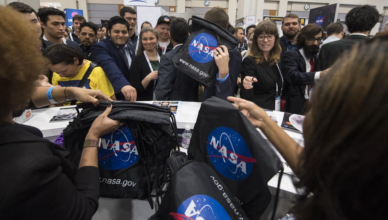 Attendees pick up NASA bags at the agency’s exhibit at the 70th International Astronautical Congress, Friday, Oct. 25, 2019, at the Walter E. Washington Convention Center in Washington.  Photo Credit: (NASA/Joel Kowsky)