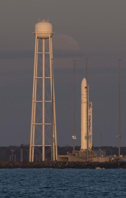 The Moon sets behind a Northrop Grumman Antares rocket carrying a Cygnus resupply spacecraft at sunrise on Pad-0A, Sunday, Feb. 9, 2020, at NASA's Wallops Flight Facility in Virginia. Northrop Grumman’s 13th contracted cargo resupply mission with NASA to the International Space Station will deliver more than 7,500 pounds of science and research, crew supplies and vehicle hardware to the orbital laboratory and its crew. The CRS-13 Cygnus spacecraft is named after the first African American astronaut, Major Robert Henry Lawrence Jr.. Photo Credit: (NASA/Aubrey Gemignani)
