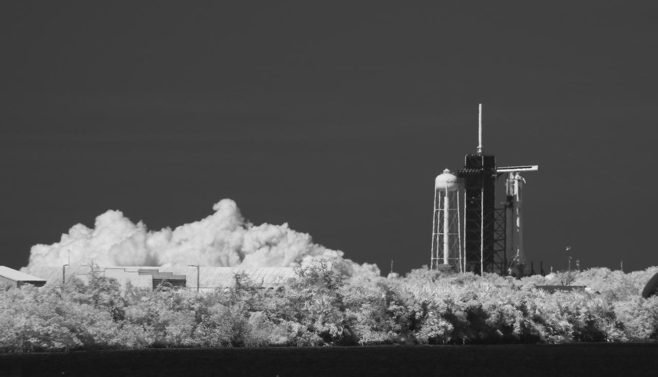 In this black and white infrared image, a SpaceX Falcon 9 rocket with the company's Crew Dragon spacecraft onboard is seen on the launch pad at Launch Complex 39A during a brief static fire test ahead of NASA’s SpaceX Demo-2 mission, Friday, May 22, 2020, at NASA’s Kennedy Space Center in Florida. NASA’s SpaceX Demo-2 mission is the first launch with astronauts of the SpaceX Crew Dragon spacecraft and Falcon 9 rocket to the International Space Station as part of the agency’s Commercial Crew Program. The test flight serves as an end-to-end demonstration of SpaceX’s crew transportation system. Robert Behnken and Douglas Hurley are scheduled to launch at 4:33 p.m. EDT on Wednesday, May 27, from Launch Complex 39A at the Kennedy Space Center. A new era of human spaceflight is set to begin as American astronauts once again launch on an American rocket from American soil to low-Earth orbit for the first time since the conclusion of the Space Shuttle Program in 2011. Photo Credit: (NASA/Joel Kowsky)