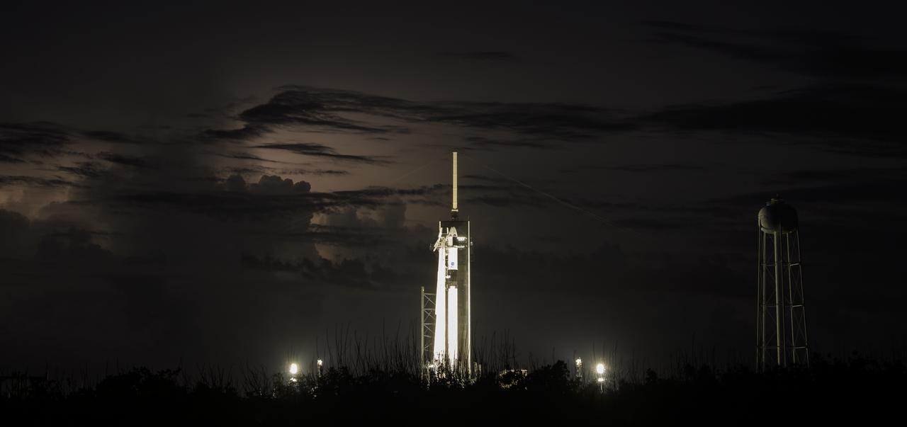 Distant storms illuminate the night sky behind a SpaceX Falcon 9 rocket with the company's Crew Dragon spacecraft onboard at Launch Complex 39A as preparations continue for the Demo-2 mission, Friday, May 29, 2020, at NASA’s Kennedy Space Center in Florida. NASA’s SpaceX Demo-2 mission is the first launch with astronauts of the SpaceX Crew Dragon spacecraft and Falcon 9 rocket to the International Space Station as part of the agency’s Commercial Crew Program. The test flight serves as an end-to-end demonstration of SpaceX’s crew transportation system. Robert Behnken and Douglas Hurley are scheduled to launch at 3:22 p.m. EDT on Saturday, May 30, from Launch Complex 39A at the Kennedy Space Center. A new era of human spaceflight is set to begin as American astronauts once again launch on an American rocket from American soil to low-Earth orbit for the first time since the conclusion of the Space Shuttle Program in 2011. Photo Credit: (NASA/Bill Ingalls)