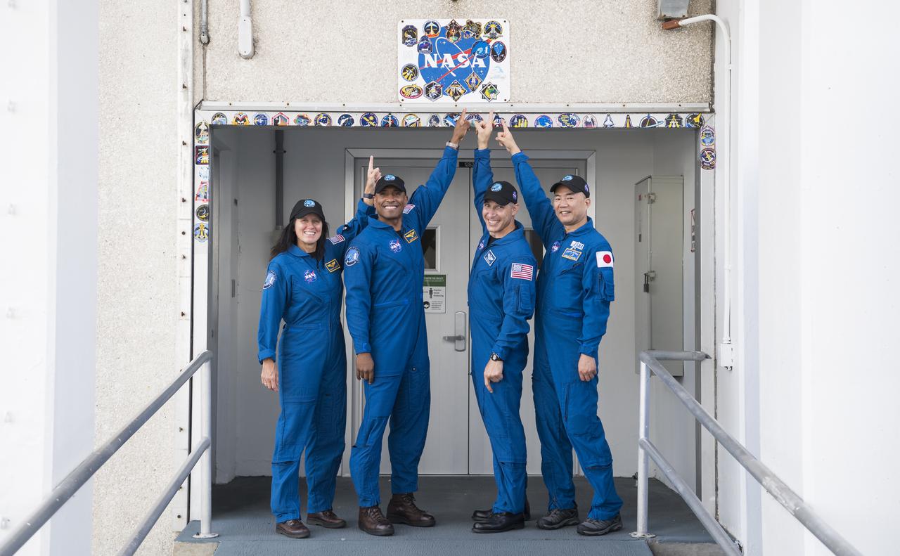 NASA astronauts Shannon Walker, left, Victor Glover, second from left, Mike Hopkins, second form right, and Japan Aerospace Exploration Agency (JAXA) astronaut Soichi Noguchi, right, pose for a picture after placing a Crew-1 mission sticker above the doorway to crew quarters at the Neil  A. Armstrong Operations and Checkout Building, Thursday, Nov. 12, 2020, at NASA’s Kennedy Space Center in Florida. NASA’s SpaceX Crew-1 mission is the first crew rotation mission of the SpaceX Crew Dragon spacecraft and Falcon 9 rocket to the International Space Station as part of the agency’s Commercial Crew Program. Glover, Noguchi, Walker, and Hopkins are scheduled to launch at 7:27 p.m. EST on Sunday, Nov. 15, from Launch Complex 39A at the Kennedy Space Center. Photo Credit: (NASA/Joel Kowsky)