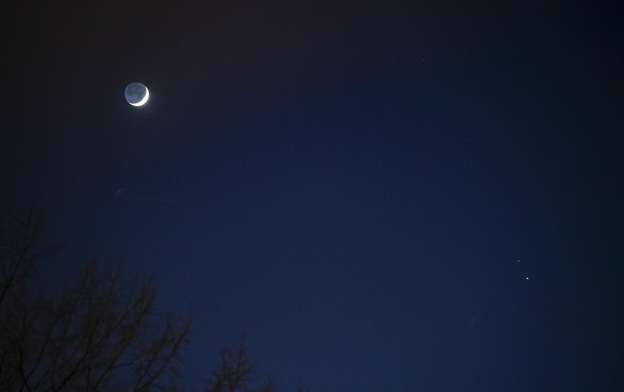 The Moon, left, Saturn, upper right, and Jupiter, lower right, are seen after sunset from Washington, DC, Thurs. Dec. 17, 2020. The two planets are drawing closer to each other in the sky as they head towards a “great conjunction” on December 21, where the two giant planets will appear a tenth of a degree apart. Photo Credit: (NASA/Aubrey Gemignani)