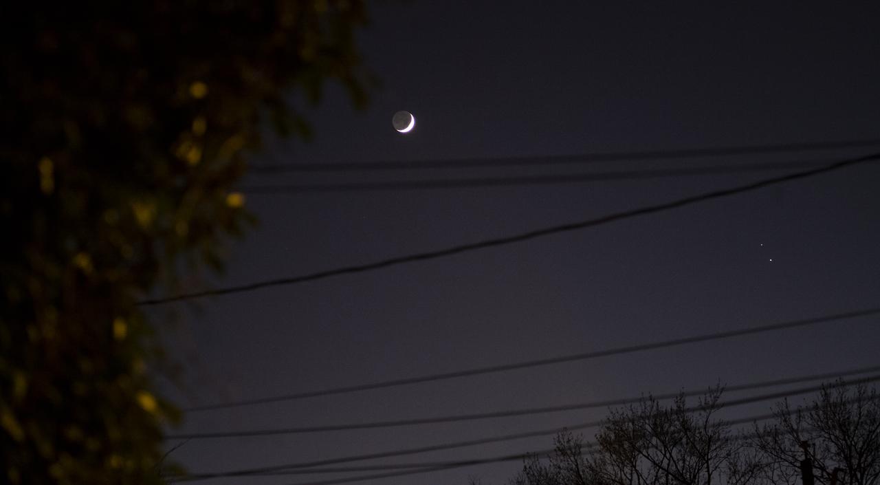 The Moon, left, Saturn, upper right, and Jupiter, lower right, are seen after sunset from Alexandria, Va., Thursday, Dec. 17, 2020. The two planets are drawing closer to each other in the sky as they head towards a “great conjunction” on December 21, where the two giant planets will appear a tenth of a degree apart. Photo Credit: (NASA/Joel Kowsky)