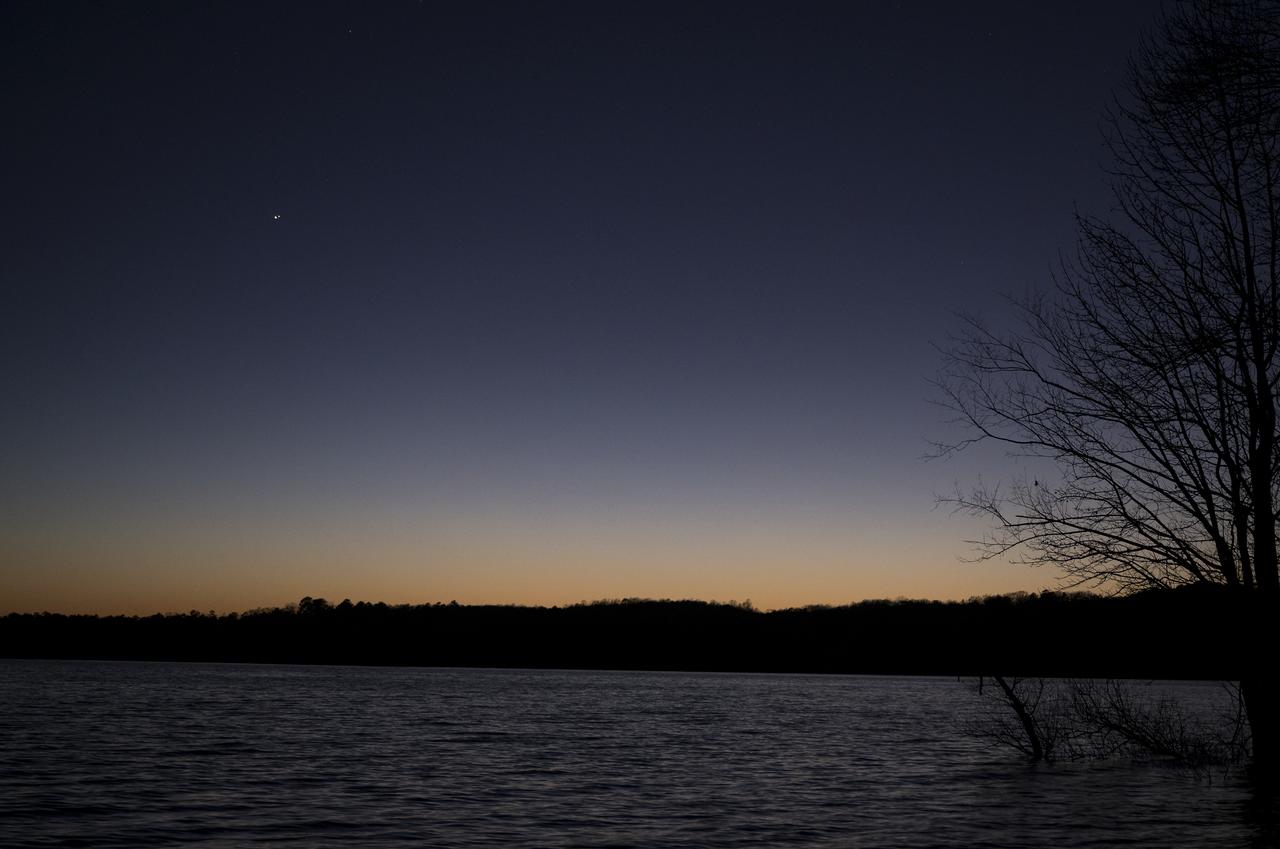 Jupiter, left, and Saturn, right, are seen after sunset above Jordan Lake during the “great conjunction” where the two planets appear a tenth of a degree apart from one another, Monday, Dec. 21, 2020, near Chapel Hill, North Carolina. Photo Credit: (NASA/Bill Ingalls)