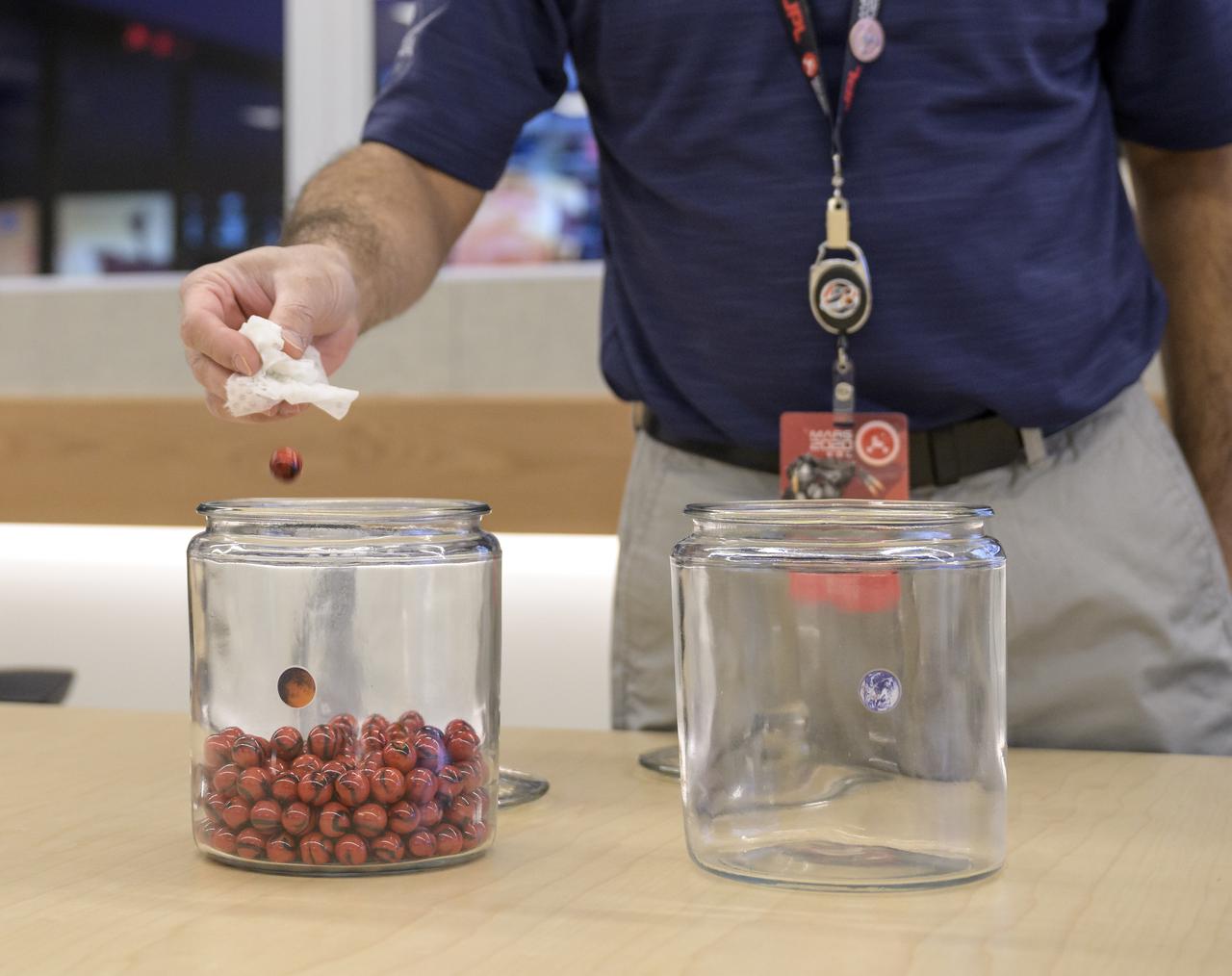 Perseverance flight director Magdy Bareh moves the final marble from the Perseverance Mars rover Earth launch jar to the Mars landing in a conference room of the Mission Support Area (MSA) Thursday, Feb. 18, 2021, at NASA's Jet Propulsion Laboratory in Pasadena, California. The Perseverance Mars rover team has been moving one marble a day since launch from jar to jar. A key objective for Perseverance’s mission on Mars is astrobiology, including the search for signs of ancient microbial life. The rover will characterize the planet’s geology and past climate, pave the way for human exploration of the Red Planet, and be the first mission to collect and cache Martian rock and regolith. Photo Credit: (NASA/Bill Ingalls)
