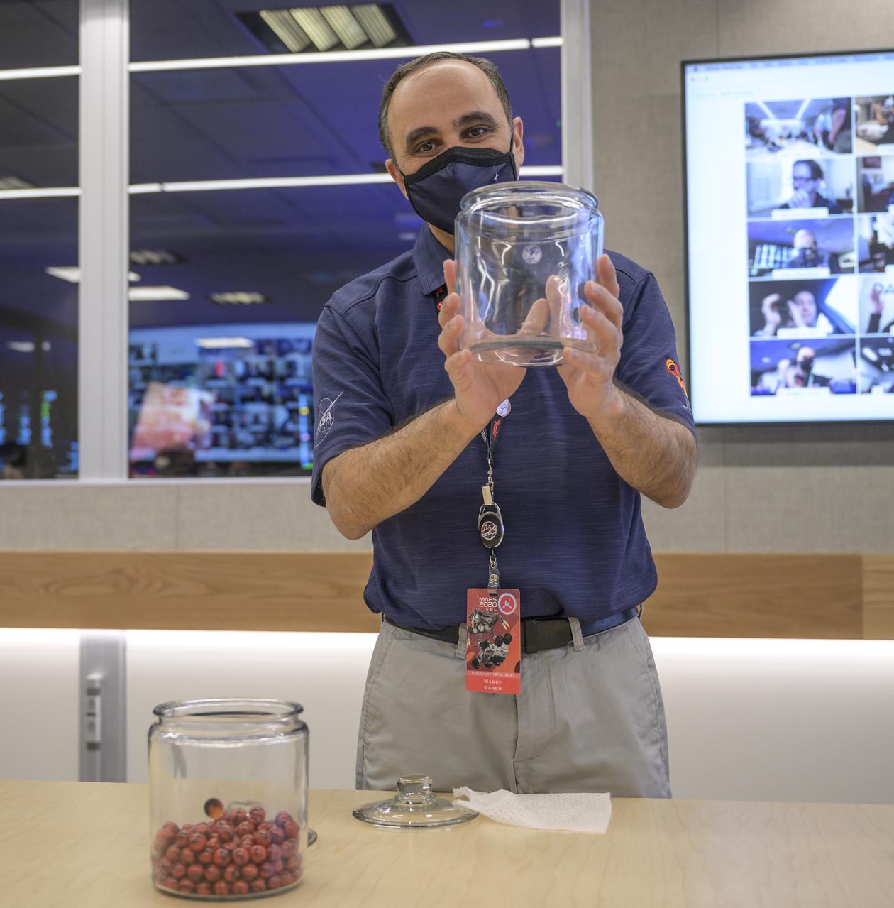 Perseverance flight director Magdy Bareh holds an empty jar after moving the final marble from the Perseverance Mars rover Earth launch jar to the Mars landing jar in a conference room of the Mission Support Area (MSA) Thursday, Feb. 18, 2021, at NASA's Jet Propulsion Laboratory in Pasadena, California. The Perseverance Mars rover team has been moving one marble a day since launch from jar to jar. A key objective for Perseverance’s mission on Mars is astrobiology, including the search for signs of ancient microbial life. The rover will characterize the planet’s geology and past climate, pave the way for human exploration of the Red Planet, and be the first mission to collect and cache Martian rock and regolith. Photo Credit: (NASA/Bill Ingalls)