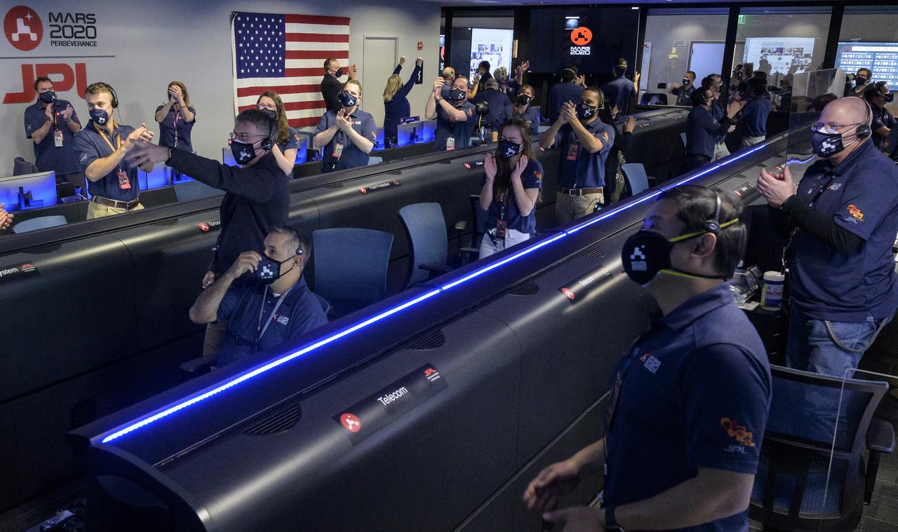 Members of NASA’s Perseverance Mars rover team watch in mission control as the first images arrive moments after the spacecraft successfully touched down on Mars, Thursday, Feb. 18, 2021, at NASA's Jet Propulsion Laboratory in Pasadena, California. A key objective for Perseverance’s mission on Mars is astrobiology, including the search for signs of ancient microbial life. The rover will characterize the planet’s geology and past climate, pave the way for human exploration of the Red Planet, and be the first mission to collect and cache Martian rock and regolith. Photo Credit: (NASA/Bill Ingalls)