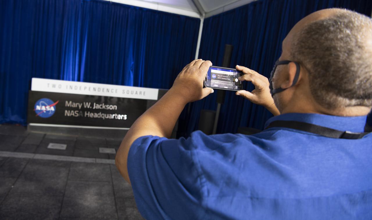 Raymond Lewis, son-in-law of Mary W. Jackson, takes a picture of the Mary W. Jackson NASA Headquarters sign following a ceremony officially naming the building, Friday, Feb. 26, 2021, at NASA Headquarters in Washington, DC. Mary W. Jackson, the first African American female engineer at NASA, began her career with the agency in the segregated West Area Computing Unit of NASA’s Langley Research Center in Hampton, Virginia. The mathematician and aerospace engineer went on to lead programs influencing the hiring and promotion of women in NASA's science, technology, engineering, and mathematics careers. In 2019, she posthumously received the Congressional Gold Medal. Photo Credit: (NASA/Joel Kowsky)