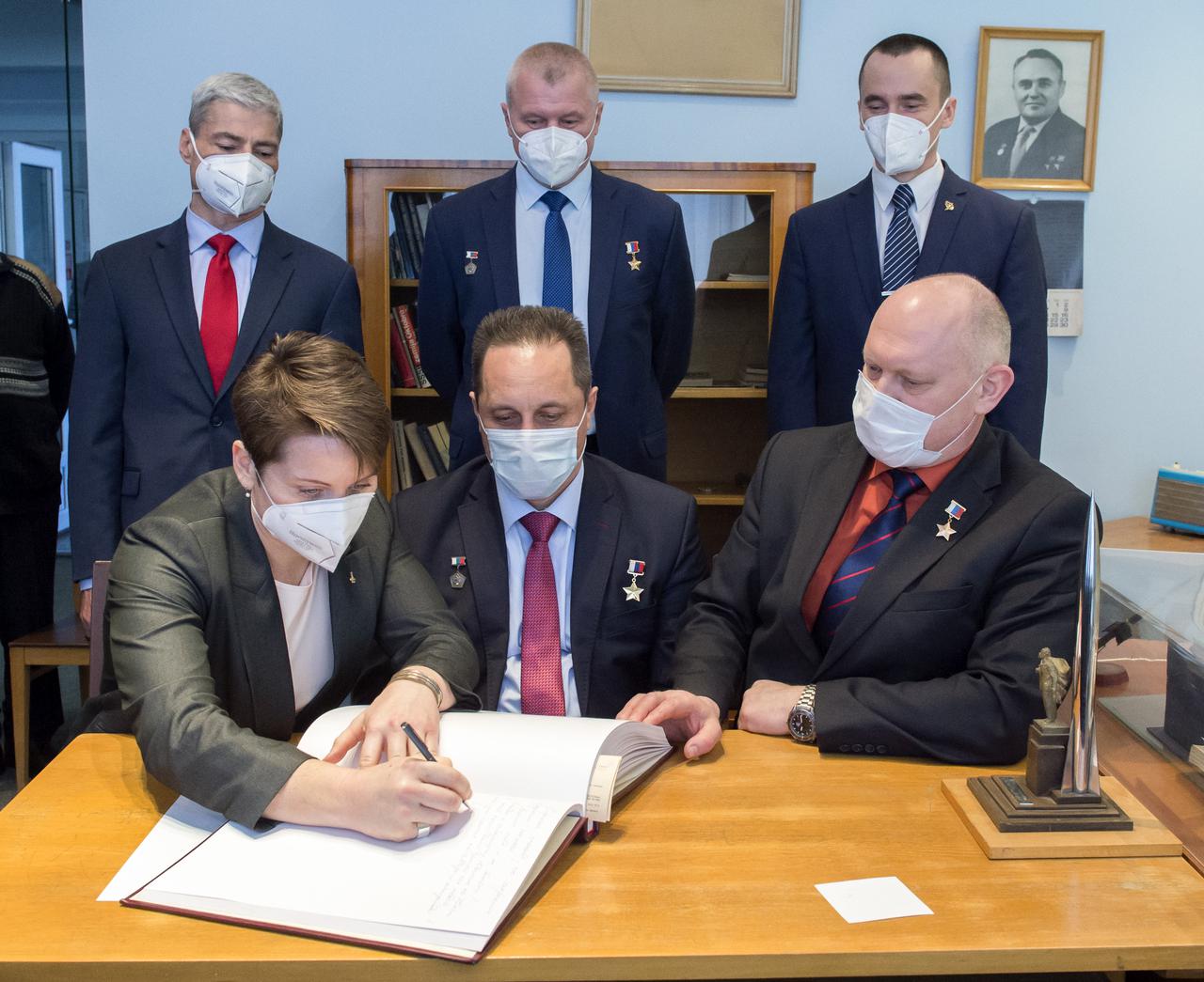 Expedition 65 backup crew member, Anne McClain of NASA signs a guest book at the "Memorial working study of Yuri Gagarin" at the Gagarin Cosmonaut Training Center (GCTC), as her crew mates watch, Wednesday, March 24, 2021 in Star City, Russia. The memorial study represents Gagarin's working study in the way it was abandoned by Gagarin on March 27, 1968 before leaving for the airfield for training flight that became his last. Photo Credit: (NASA/GCTC/Irina Spector)