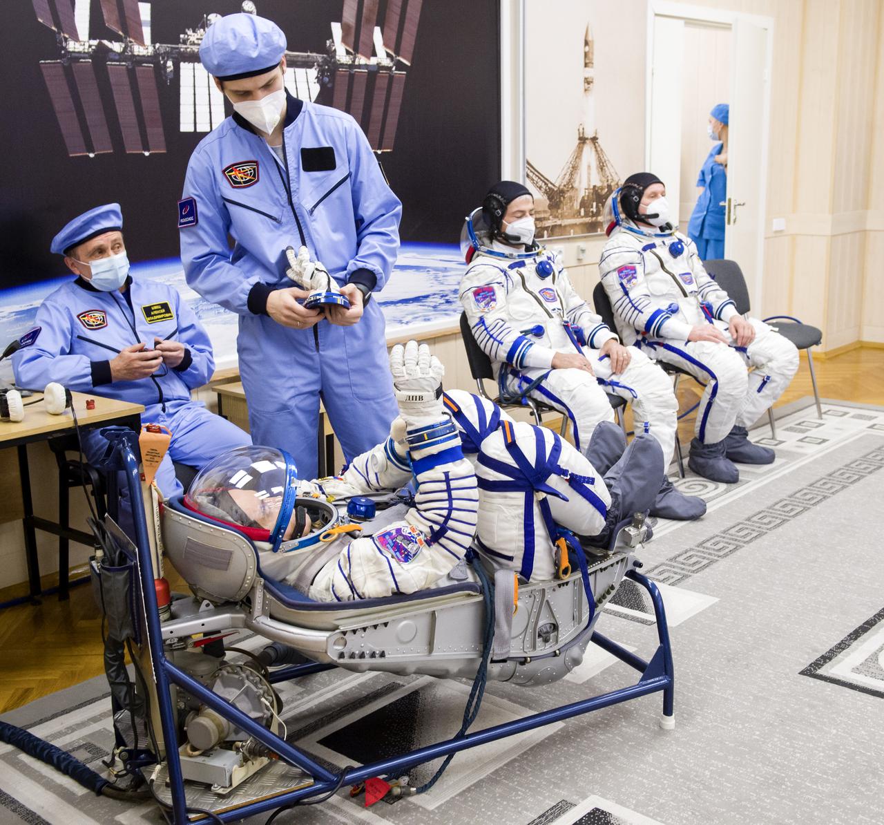 Expedition 65 prime crew member Pyotr Dubrov of Roscosmos, left, has his Sokol suit pressure checked while fellow crew mates, NASA astronaut Mark Vande Hei, center, and Russian cosmonaut Oleg Novitskiy of Roscosmos look on, during a fit check to prepare for launch, Saturday, March 27, 2021 at the Baikonur Cosmodrome in Kazakhstan. They are scheduled to launch on a Soyuz rocket April 9. Photo Credit: (NASA/GCTC/Irina Spector)