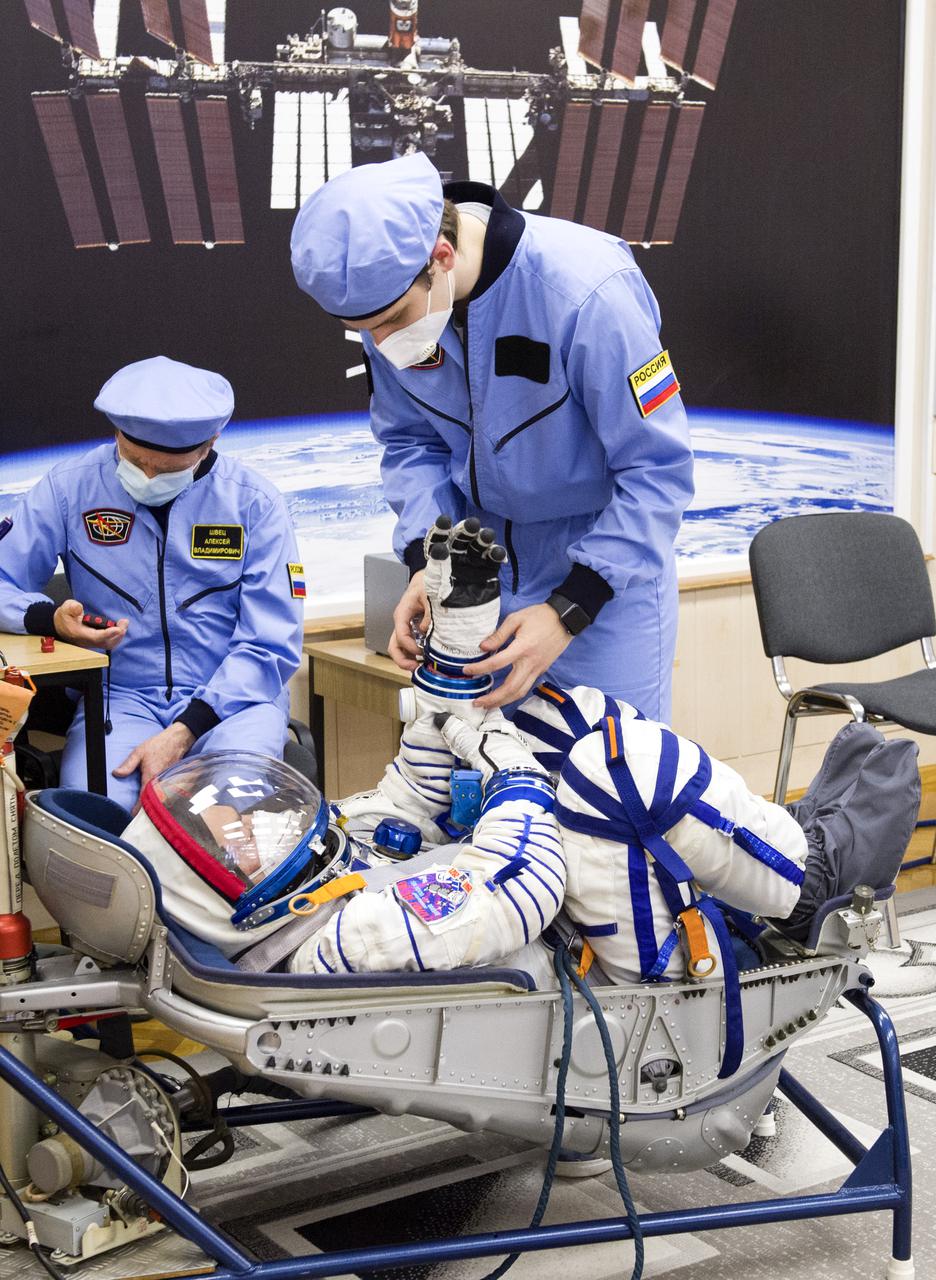 Expedition 65 prime crew member Mark Vande Hei of NASA is assisted with his glove during a Sokol suit pressure check to prepare for launch with crew mates Russian cosmonauts Oleg Novitskiy of Roscosmos and Pyotr Dubrov of Roscosmos, Saturday, March 27, 2021 at the Baikonur Cosmodrome in Kazakhstan. They are scheduled to launch on a Soyuz rocket April 9. Photo Credit: (NASA/GCTC/Irina Spector)
