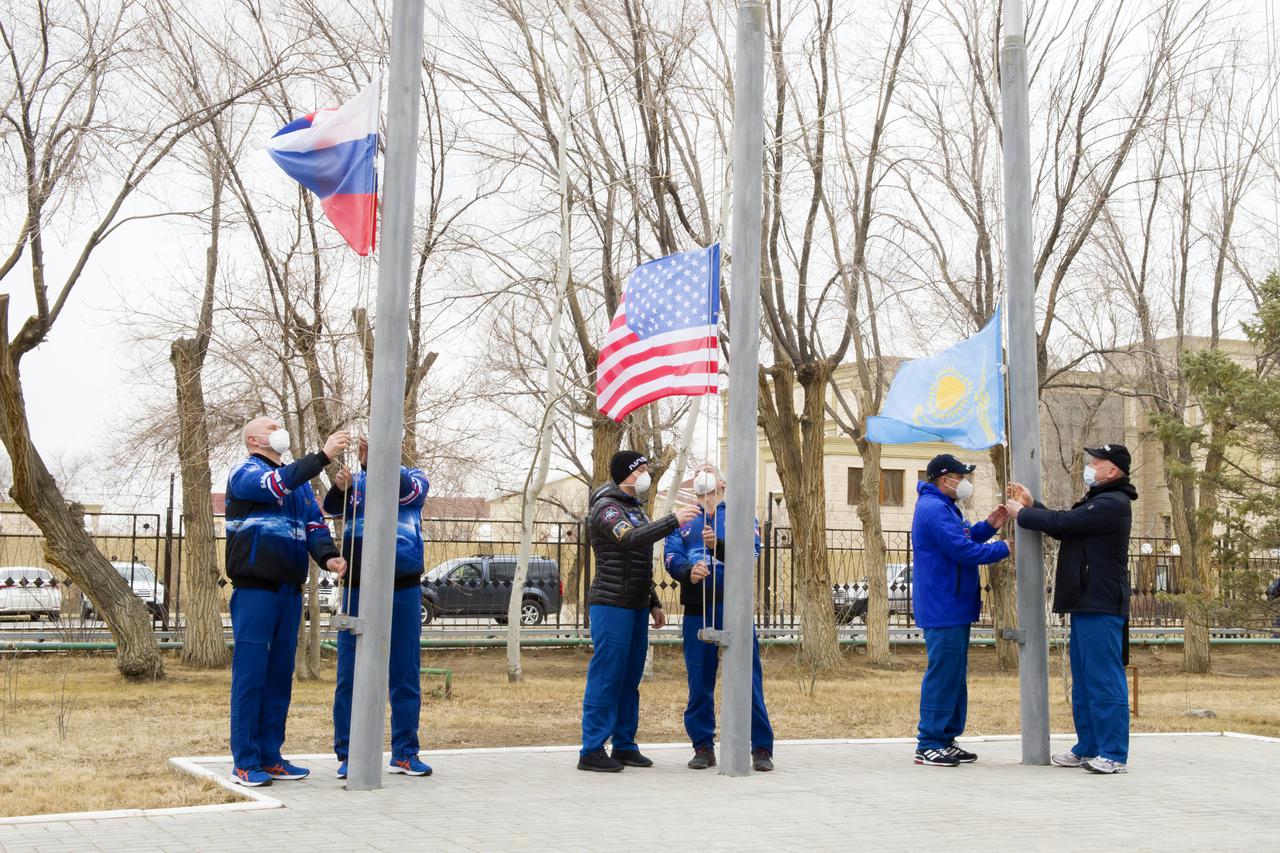 Expedition 65 prime and backup crew members raise the flags of Russia, the United States, and Kazakhstan, Sunday, March 28, 2021, in traditional ceremonies outside the Cosmonaut Hotel in Baikonur, Kazakhstan. From left to right, Expedition 65 prime crew member Oleg Novitskiy of Roscosmos and backup crew member Pyotr Dubrov of Roscosmos, Expedition 65 backup crew member, NASA astronaut Anne McClain and prime crew NASA astronaut Mark Vande Hei, and Expedition 65 backup crew cosmonaut Anton Shkaplerov of Roscosmos and prime crew cosmonaut Oleg Artemyev of Roscosmos. The prime crew is scheduled to launch to the International Space Station on a Soyuz rocket April 9. Photo Credit: (NASA/GCTC/Irina Spector)