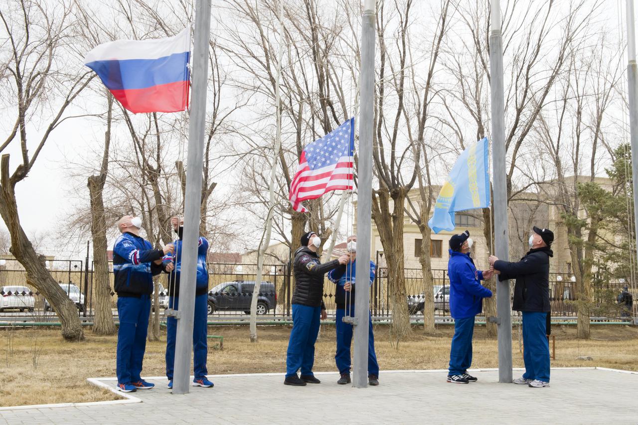 Expedition 65 prime and backup crew members raise the flags of Russia, the United States, and Kazakhstan, Sunday, March 28, 2021, in traditional ceremonies outside the Cosmonaut Hotel in Baikonur, Kazakhstan. From left to right, Expedition 65 prime crew member Oleg Novitskiy of Roscosmos and backup crew member Pyotr Dubrov of Roscosmos, Expedition 65 backup crew member, NASA astronaut Anne McClain and prime crew NASA astronaut Mark Vande Hei, and Expedition 65 backup crew cosmonaut Anton Shkaplerov of Roscosmos and prime crew cosmonaut Oleg Artemyev of Roscosmos. The prime crew is scheduled to launch to the International Space Station on a Soyuz rocket April 9. Photo Credit: (NASA/GCTC/Irina Spector)