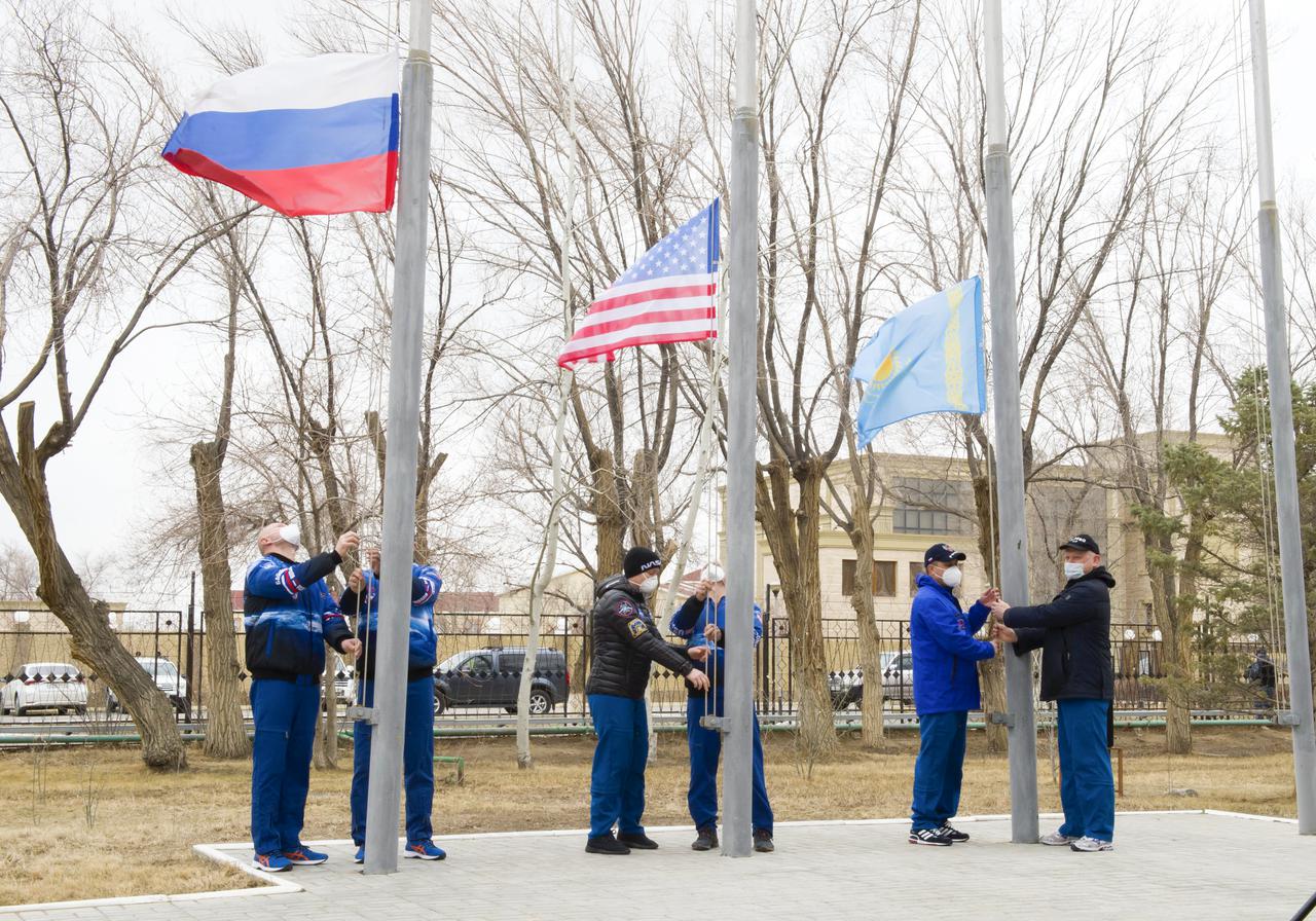 Expedition 65 prime and backup crew members raise the flags of Russia, the United States, and Kazakhstan, Sunday, March 28, 2021, in traditional ceremonies outside the Cosmonaut Hotel in Baikonur, Kazakhstan. From left to right, Expedition 65 prime crew member Oleg Novitskiy of Roscosmos and backup crew member Pyotr Dubrov of Roscosmos, Expedition 65 backup crew member, NASA astronaut Anne McClain and prime crew NASA astronaut Mark Vande Hei, and Expedition 65 backup crew cosmonaut Anton Shkaplerov of Roscosmos and prime crew cosmonaut Oleg Artemyev of Roscosmos. The prime crew is scheduled to launch to the International Space Station on a Soyuz rocket April 9. Photo Credit: (NASA/GCTC/Irina Spector)