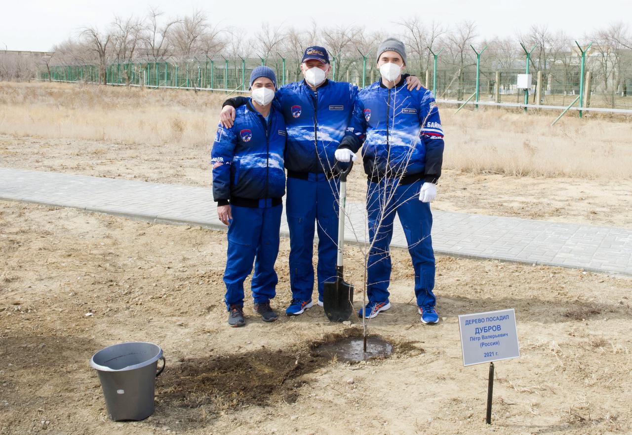 Expedition 65 prime crew members NASA astronaut Mark Vande Hei, left, and Russian cosmonauts Pyotr Dubrov, center, and Oleg Novitskiy of Roscosmos, pose for a photo after Dubrov planted a tree bearing his name as part of traditional pre-launch activities, Saturday, April 3, 2021, at the Cosmonaut Hotel in Baikonur, Kazakhstan. The trio are scheduled to launch to the International Space Station aboard the Soyuz MS-18 spacecraft on April 9. Photo Credit: (NASA/GCTC/Irina Spector)