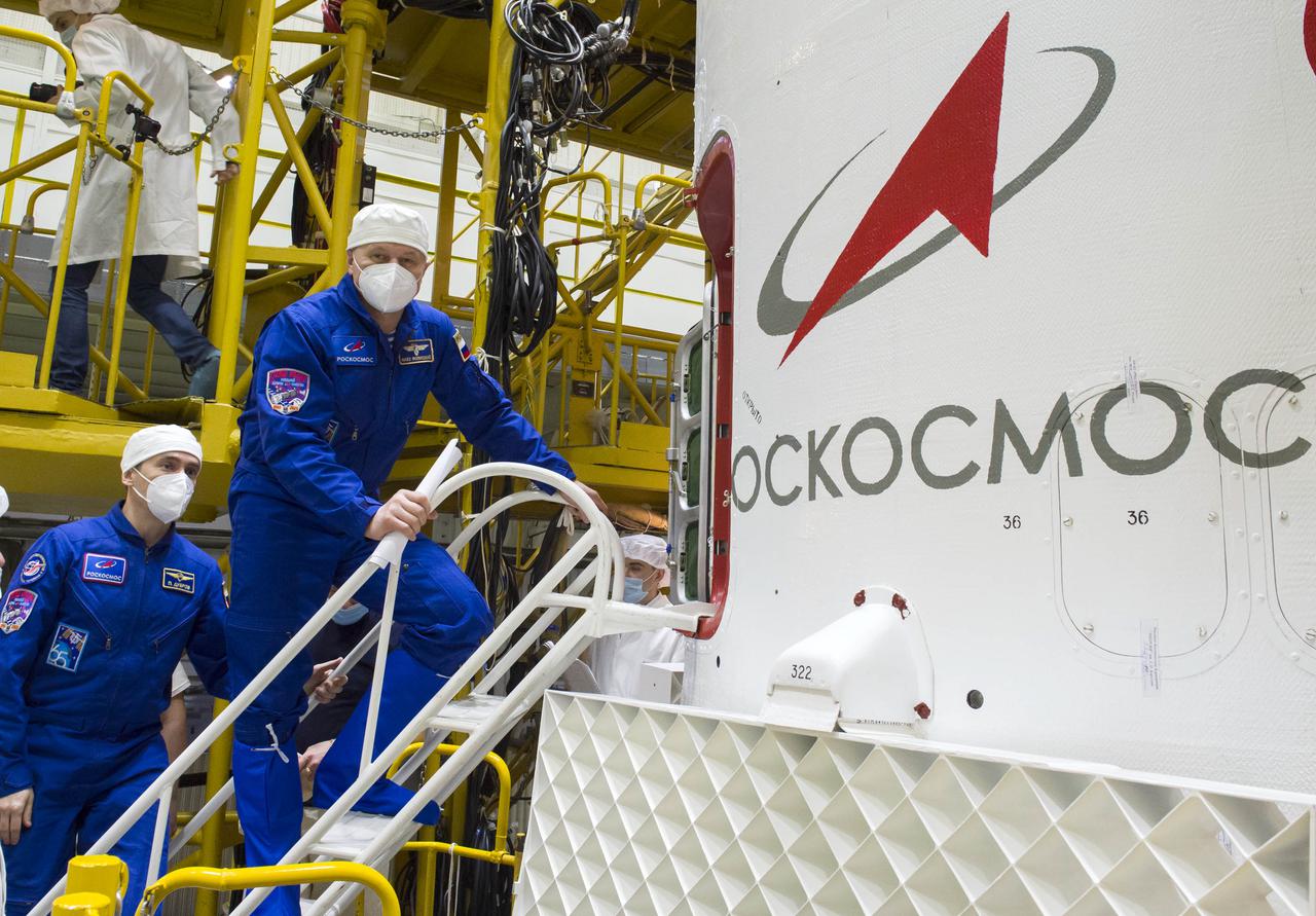 Expedition 65 prime crew member Oleg Novitskiy of Roscosmos, right, pauses for a photo as he climbs inside the Soyuz MS-18 spacecraft during the final fit check to prepare for launch with fellow Russian cosmonaut Pyotr Dubrov of Roscosmos, left, and NASA astronaut Mark Vande Hei, Sunday, April 4, 2021 at the Baikonur Cosmodrome in Kazakhstan. The trio are scheduled to launch to the International Space Station on a Soyuz rocket April 9. Photo Credit: (NASA/GCTC/Irina Spector)